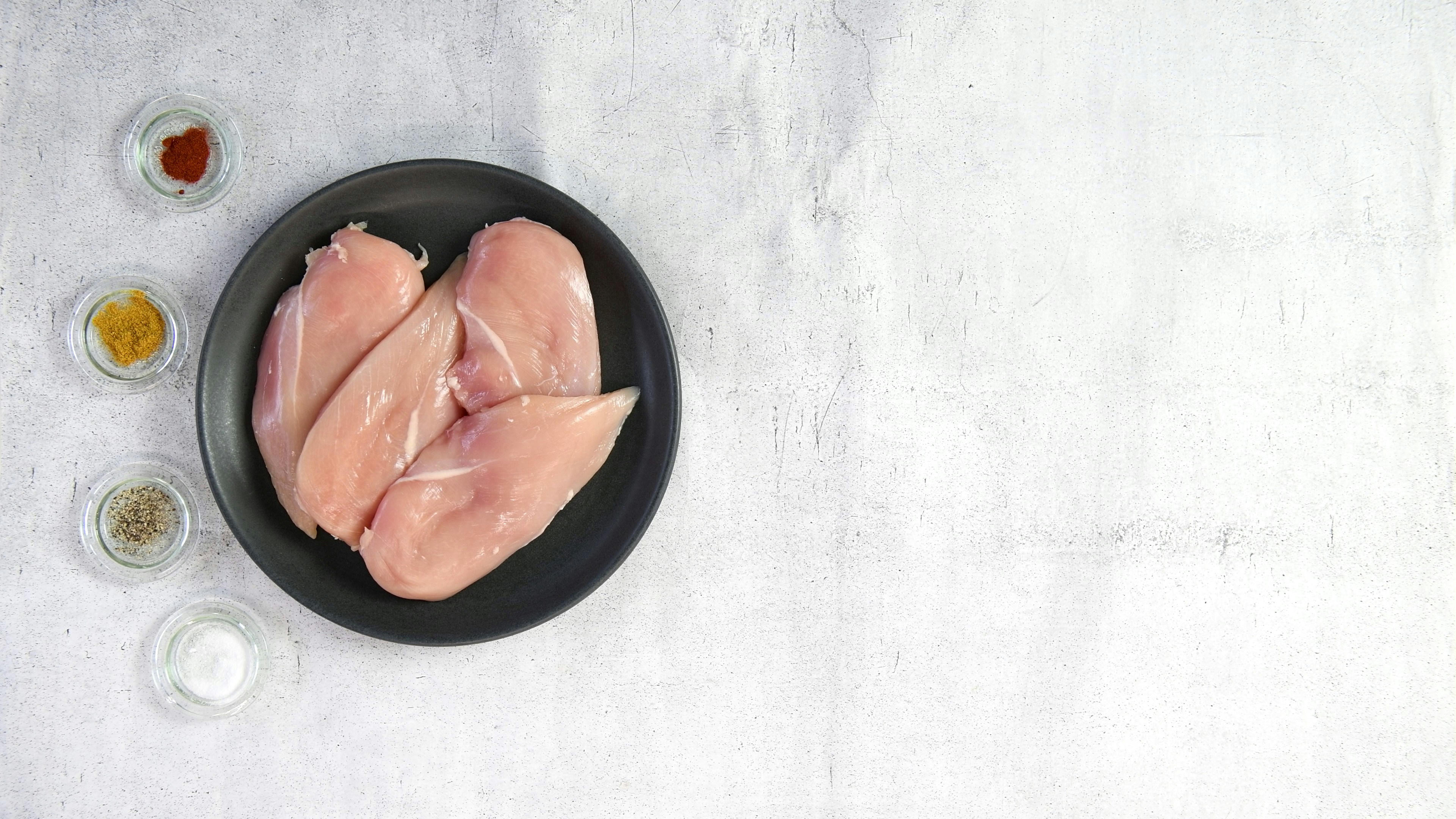 Raw Chicken Breast in a Bowl With seasoning to the side