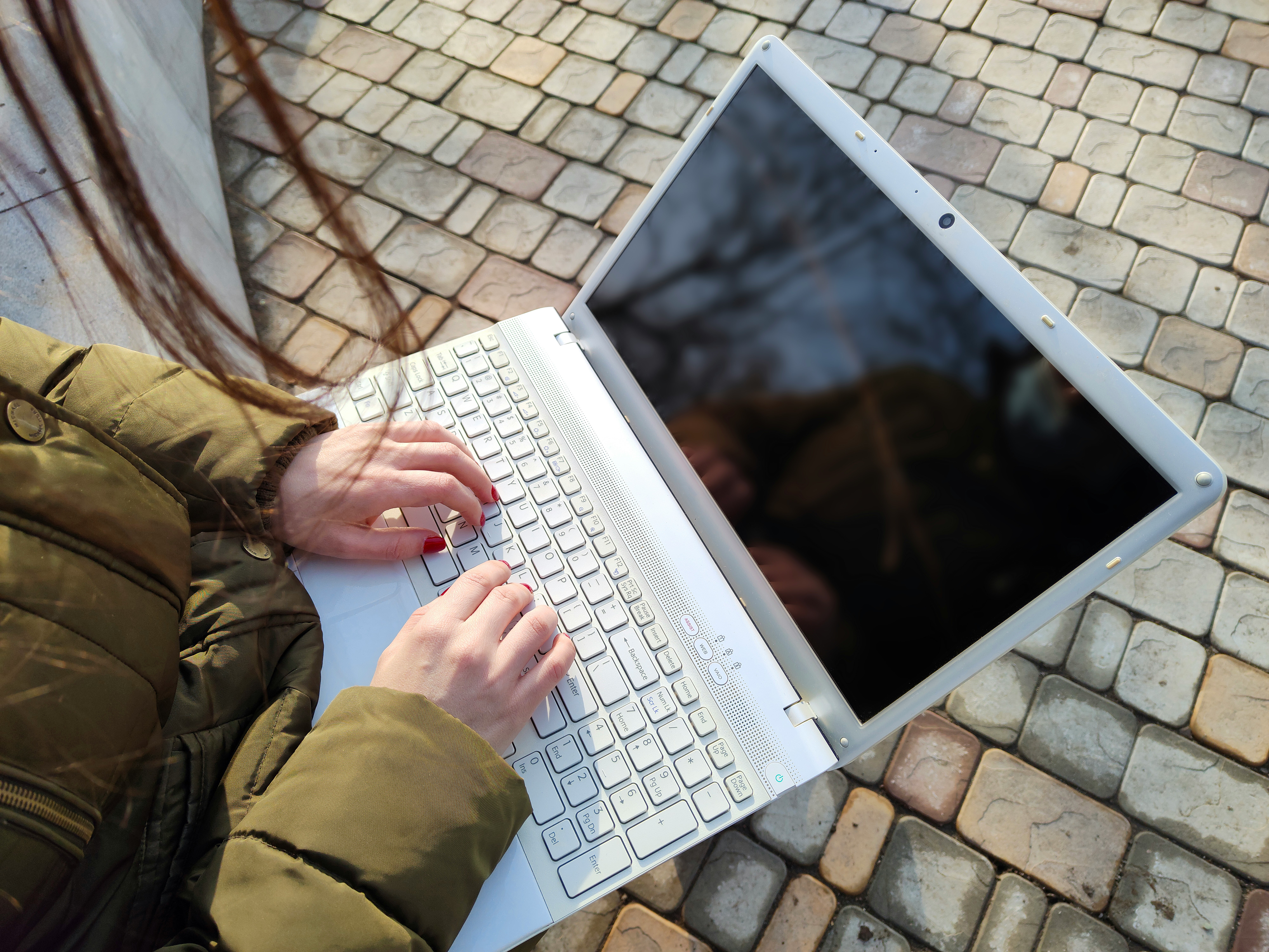 a woman is typing on a laptop outside