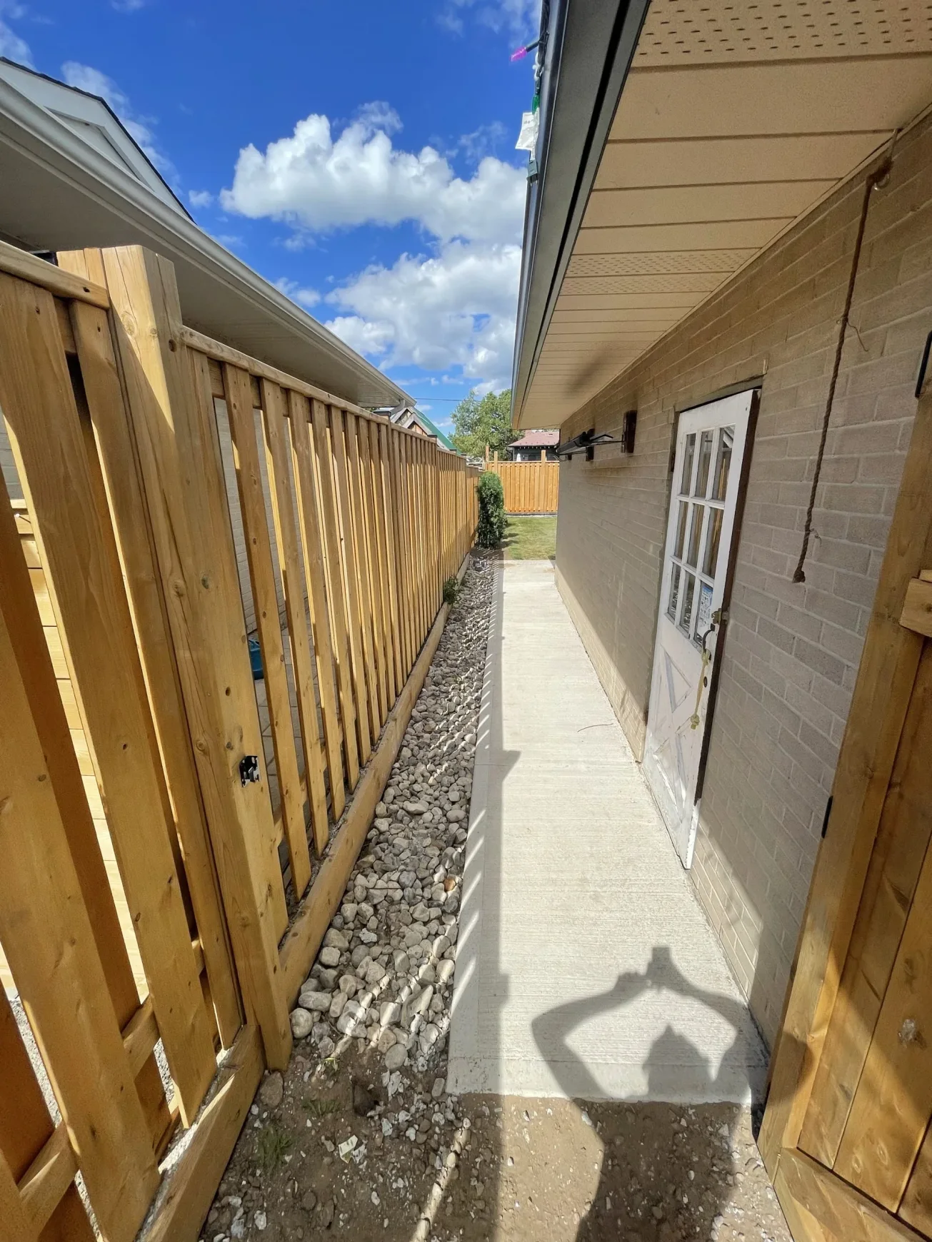 Freshly installed concrete pathway running alongside a house and wooden fence by Falcons Landscaping.