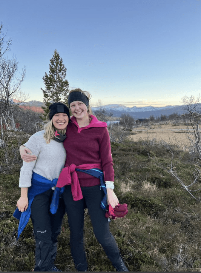Two female trainees at Aneo are on a trip together in the fall and smile at the camera