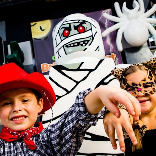 Due bambini in costume, un cowboy e un leopardo, posano davanti a una decorazione di Halloween con una mummia e un ragno.