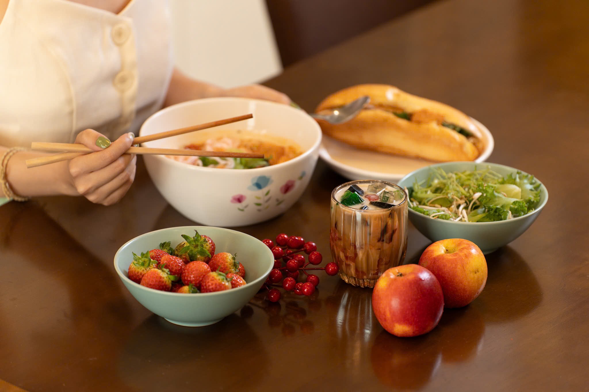A rustic outdoor market stall displays an array of fresh produce including vibrant tomatoes, leafy greens, and a variety of olives, set against the backdrop of a picturesque rural Italian village.