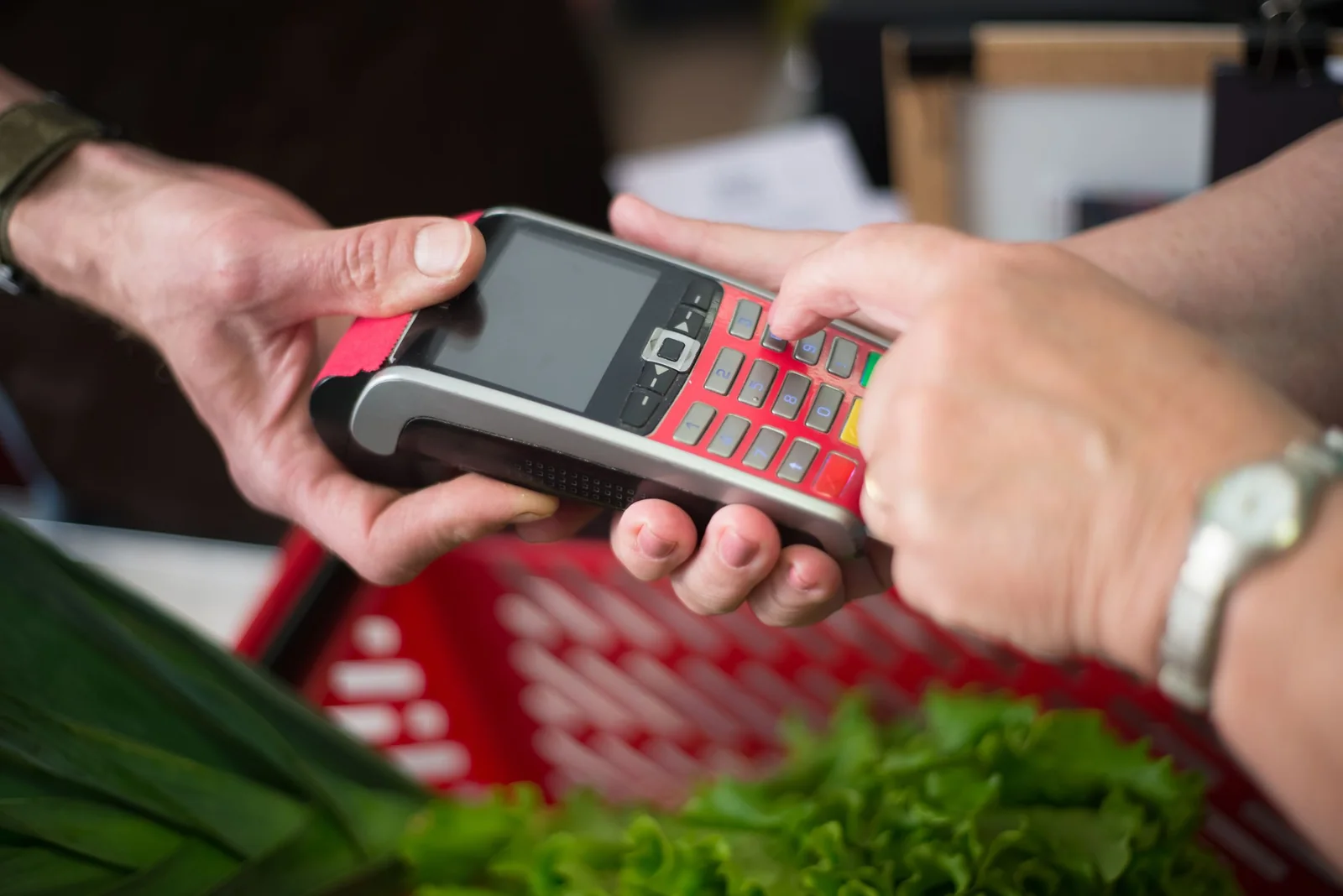 A shopper enters a PIN on a card terminal beside fresh groceries at checkout.