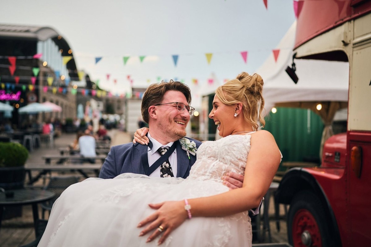 Groom carrying the bride through the Holmes Mill courtyard under colourful bunting