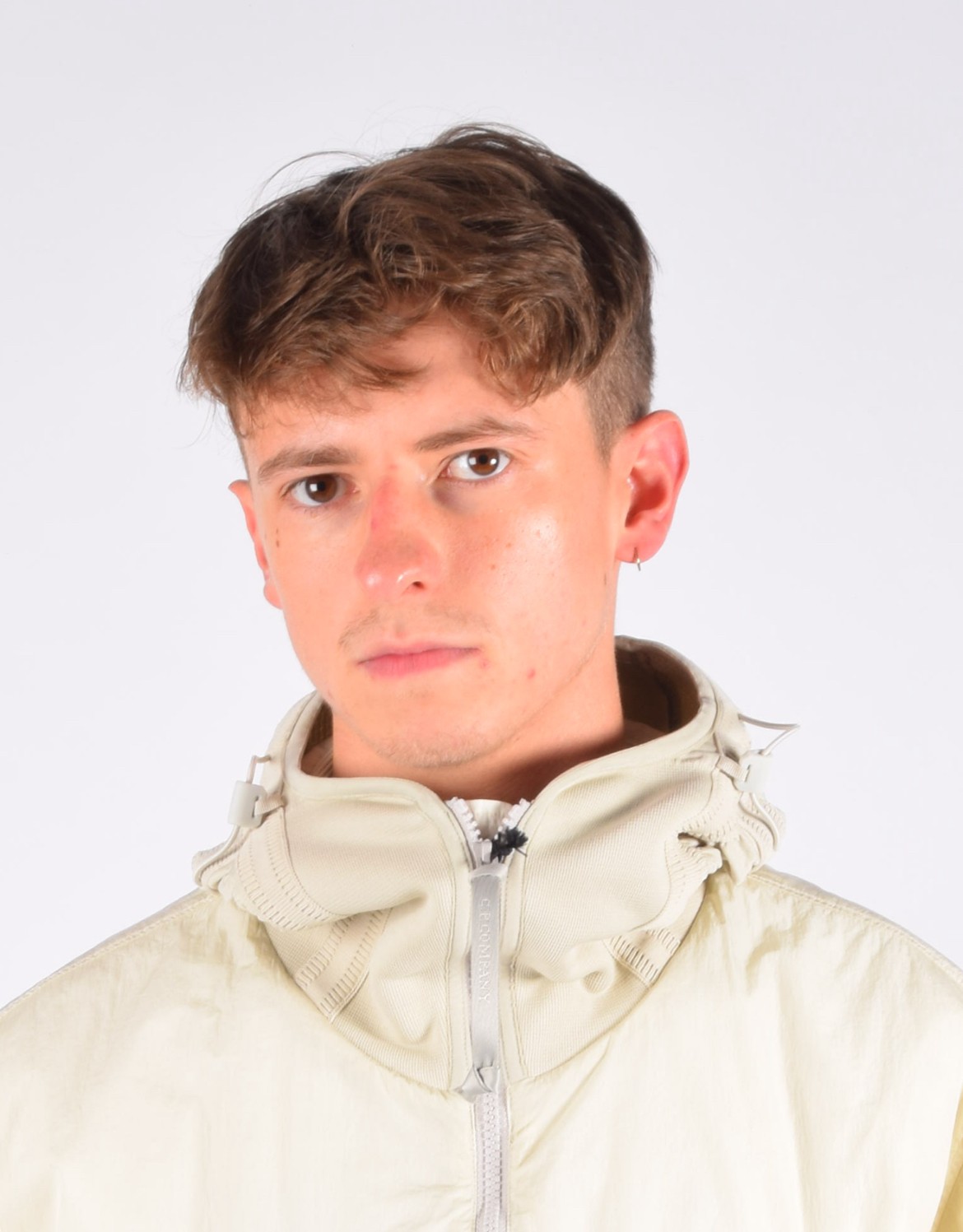 Person wearing a blue puffer jacket and red backpack standing in front of a light blue building on a city street.