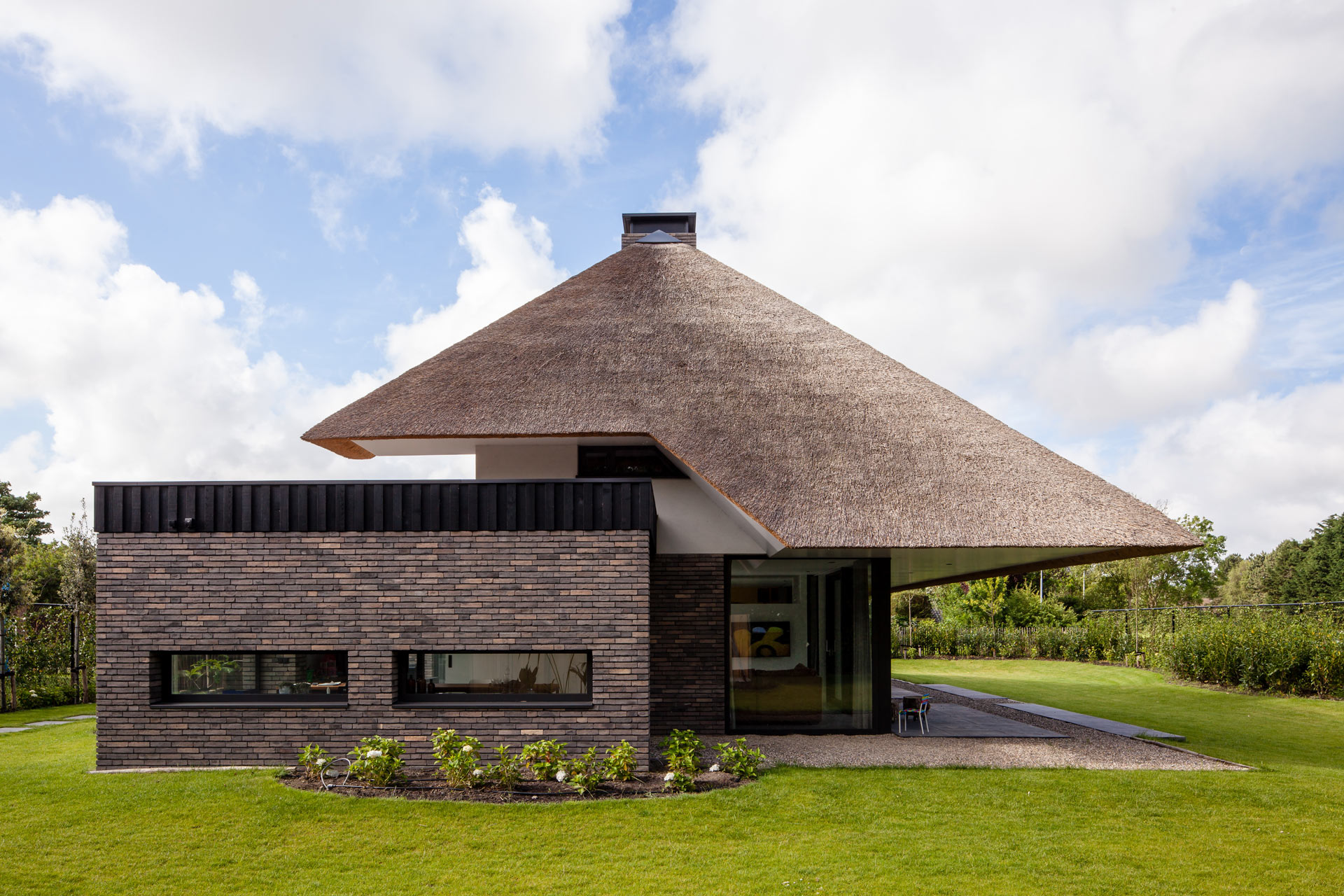 Modern huis met rieten dak en bakstenen muur in groene omgeving.