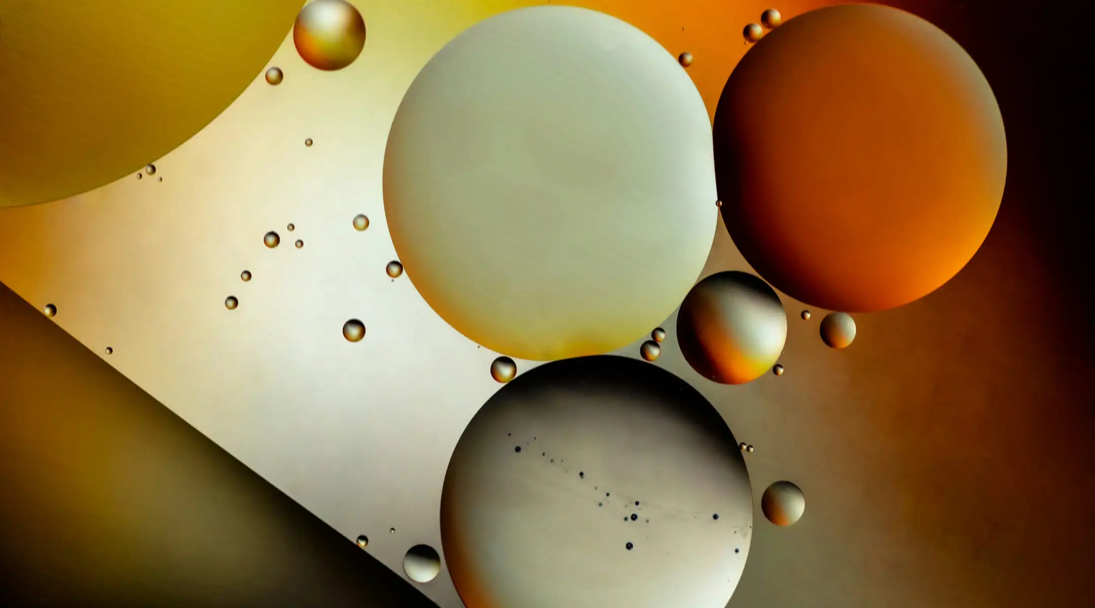 Abstract composition of large and small circular spheres in shades of white, gold, and grey over a warm, dark gradient background.