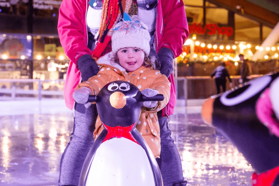 A young girl ice skating with a penguin support skate on the ice rink