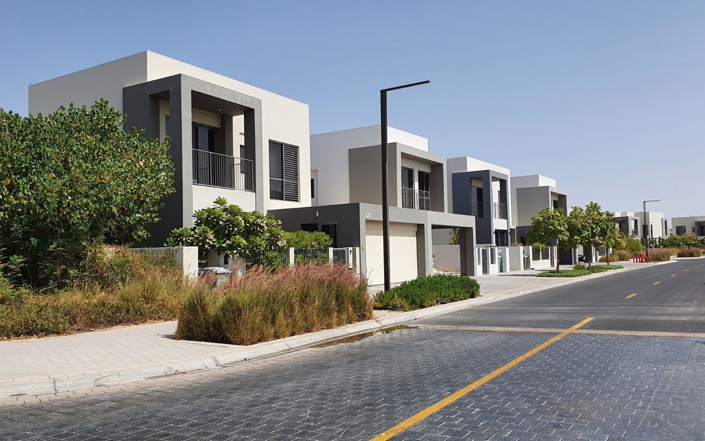 Modern Dubai Hills Estate home with clean lines, landscaped sidewalk, and clear blue sky on a quiet street.