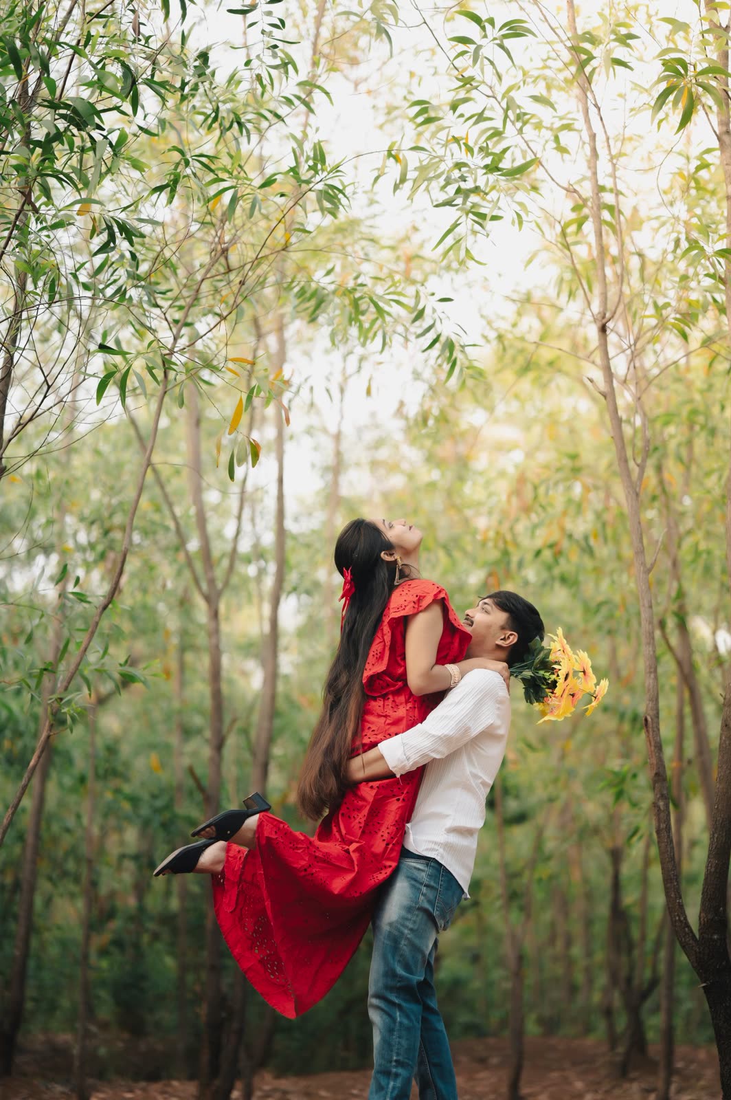 Man lifting a woman in a red dress off the ground in a forest