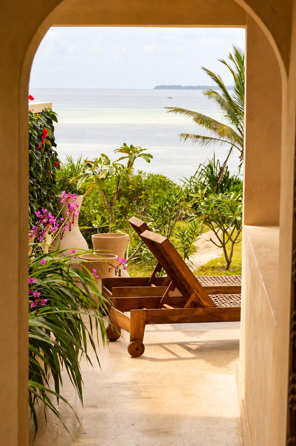 Carved wooden door and Swahili-style plasterwork detail on Villa Jua's exterior, framed by a palm plant.