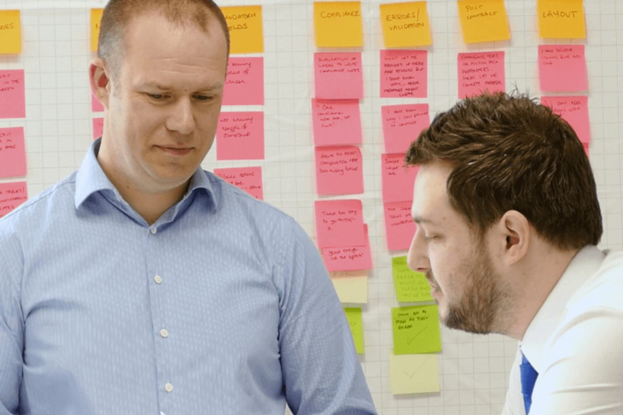Two people having a discussion in front of a wall covered in brightly coloured notes