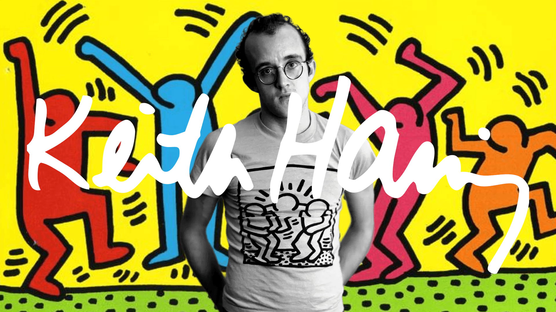 Keith Haring stands in front of a mural of dancing figures with his name written across the image.