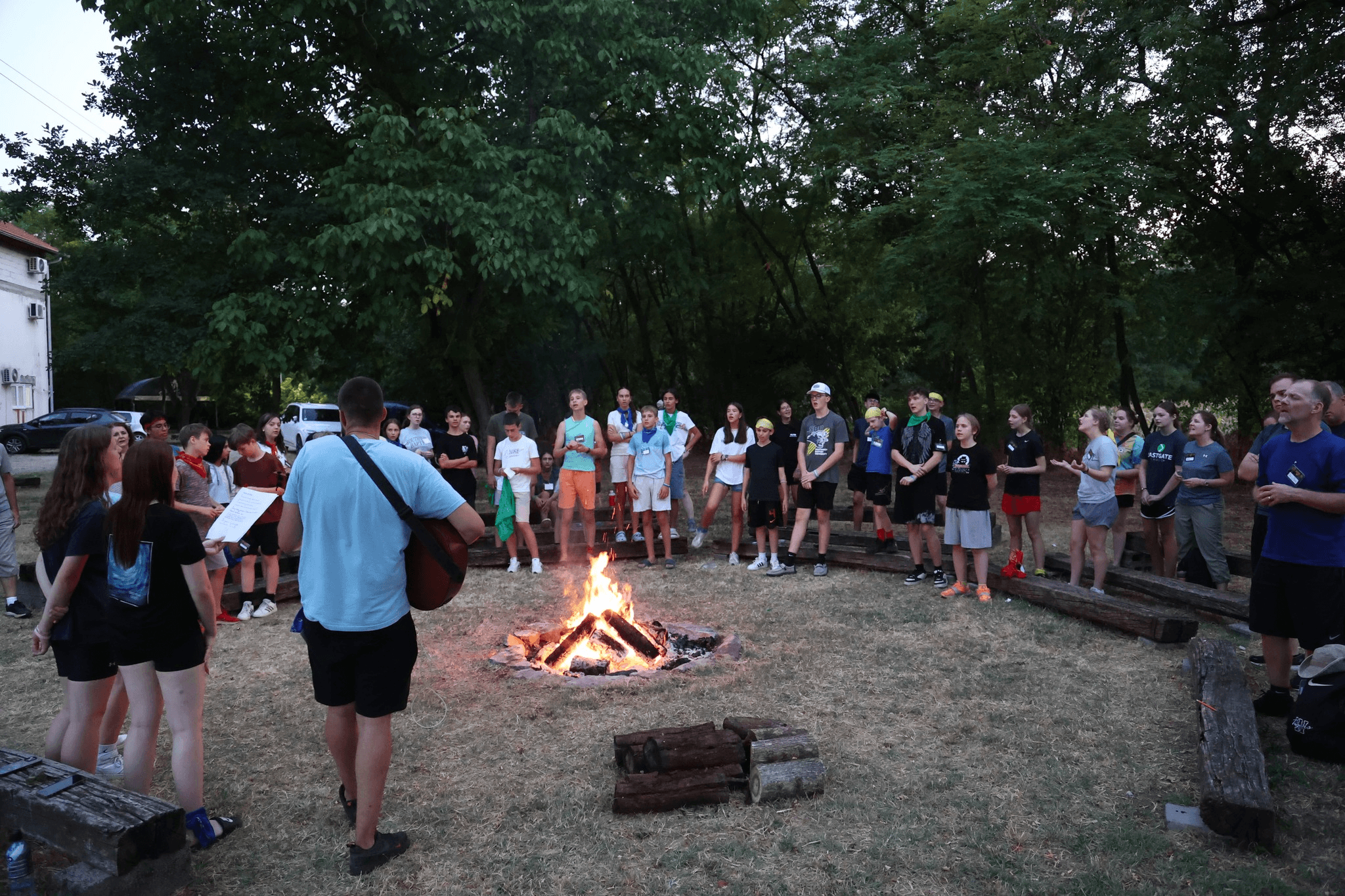 Kids are sitting and standing next to the camp fire