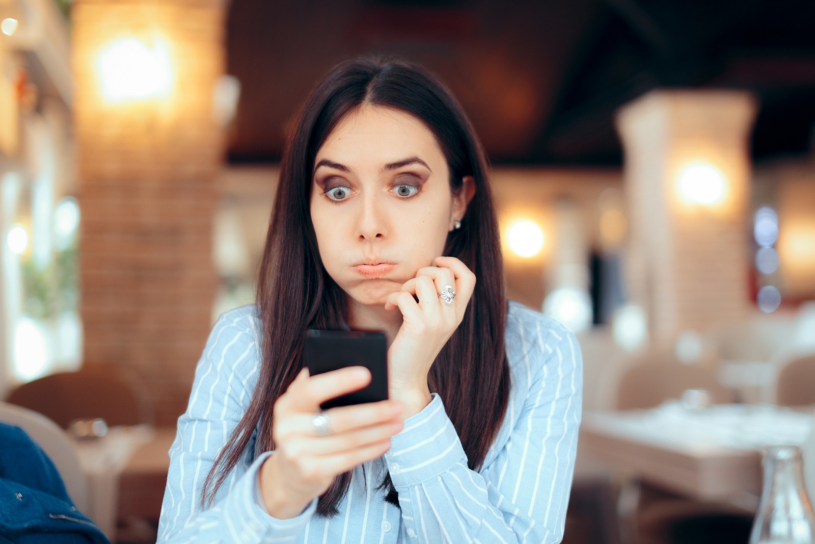 A woman looking at her phone with a shocked and uncomfortable expression.