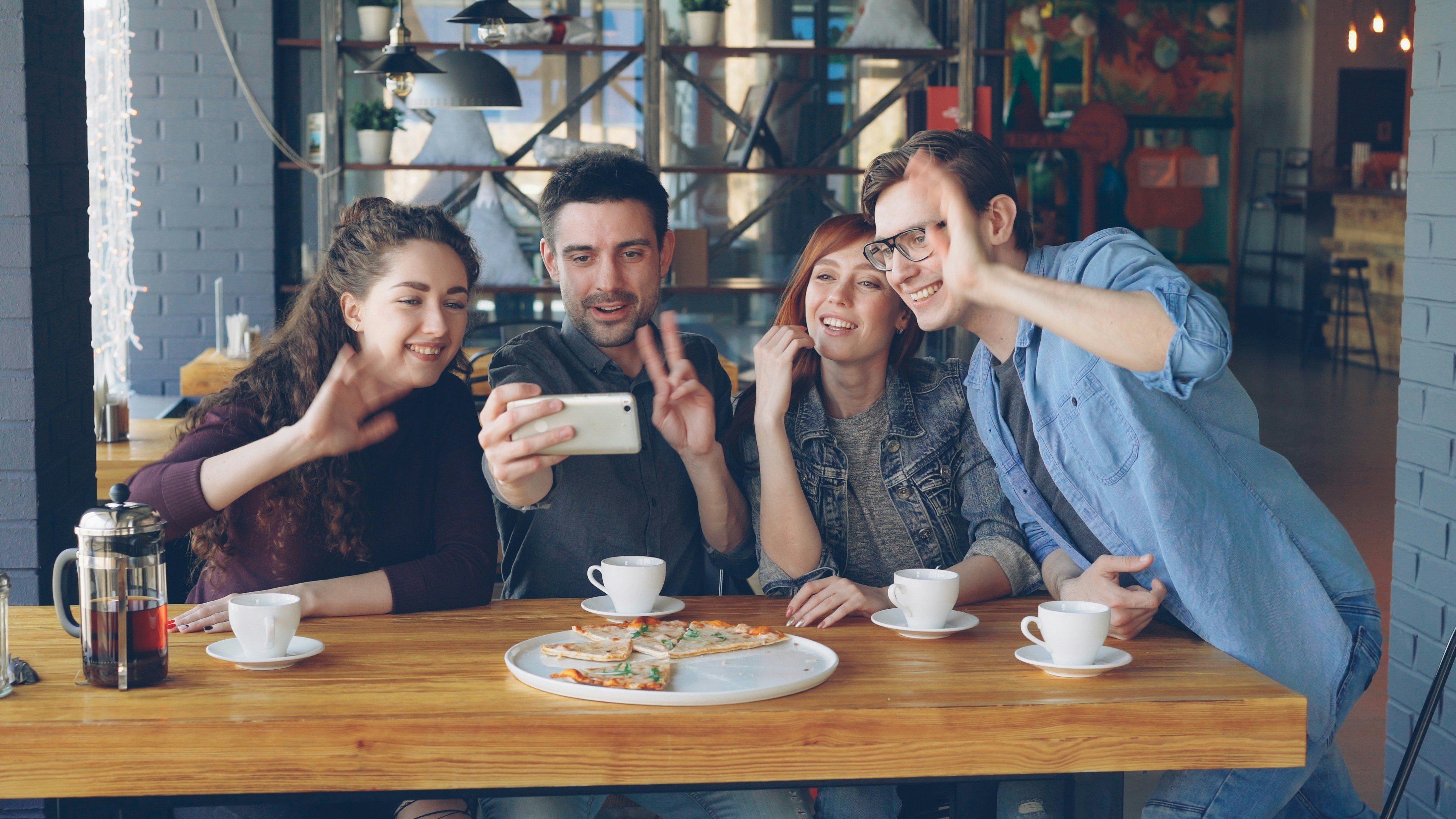 Friends smile and take a selfie at a cafe.
