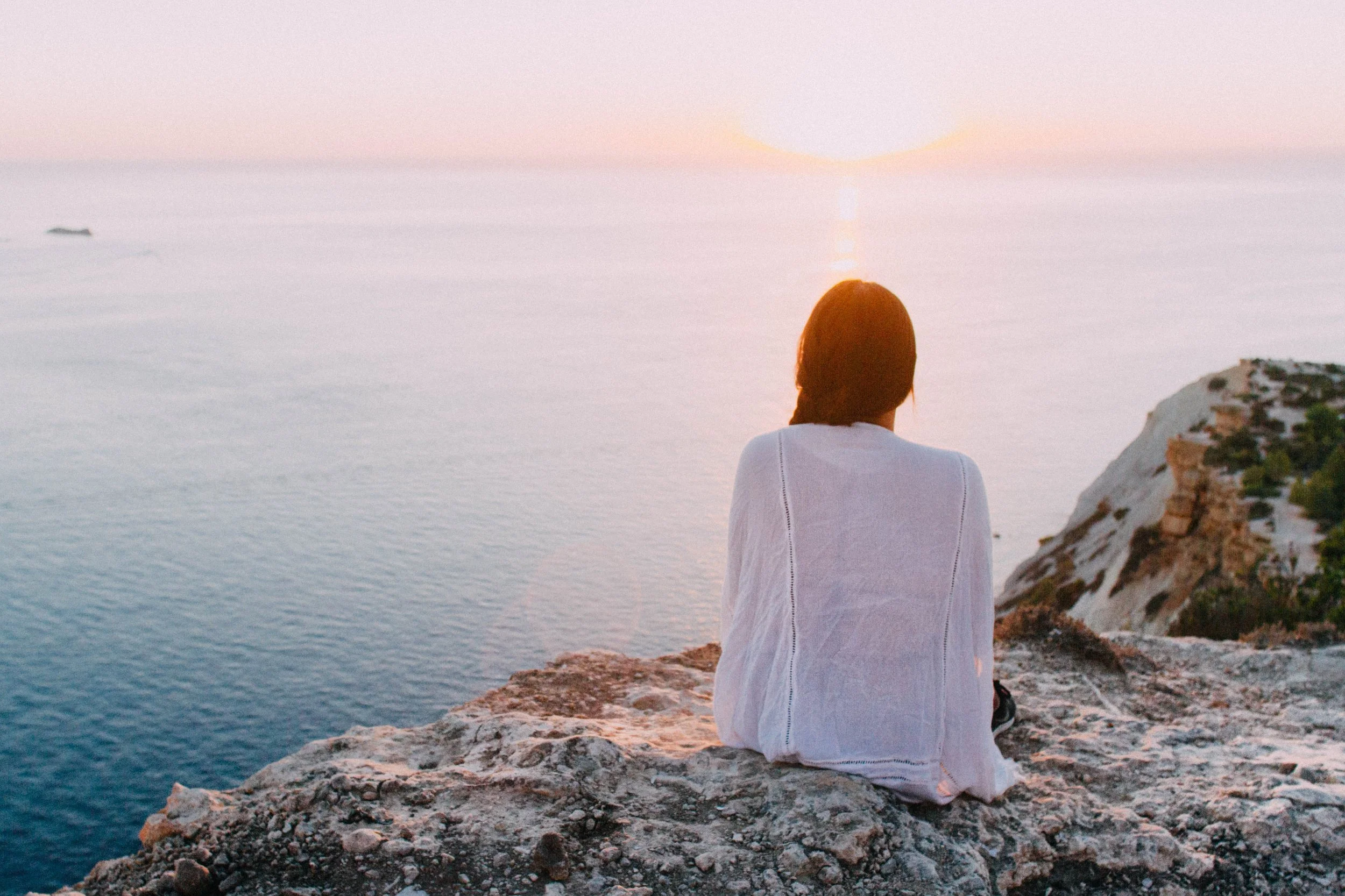 A woman practices mental health self-care as she appreciates a seaside sunset