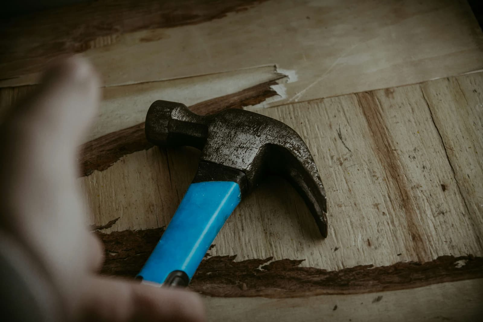 Stretched hand towards a hammer with blue handle.