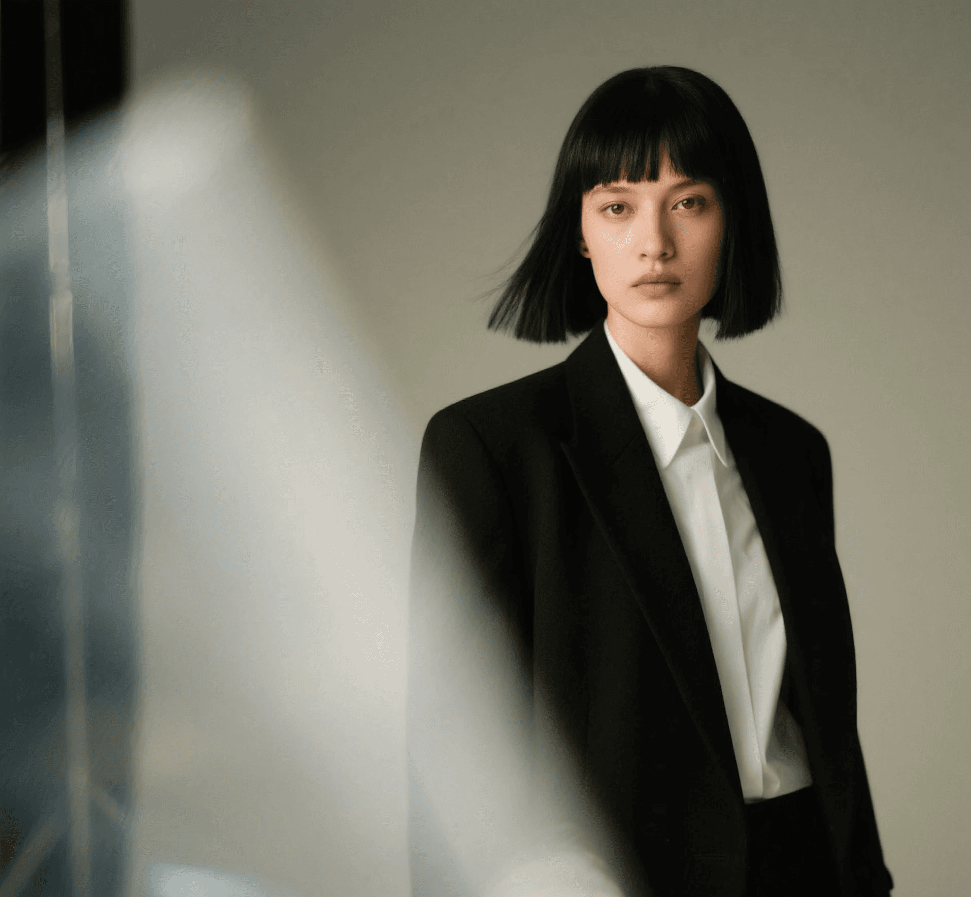 Stylish individual in a black blazer and white shirt, with a soft focus effect adding an artistic touch to the neutral background.