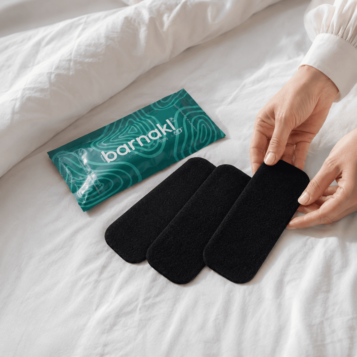 Three Barnakl filters and their teal package being unpacked on white bed linen