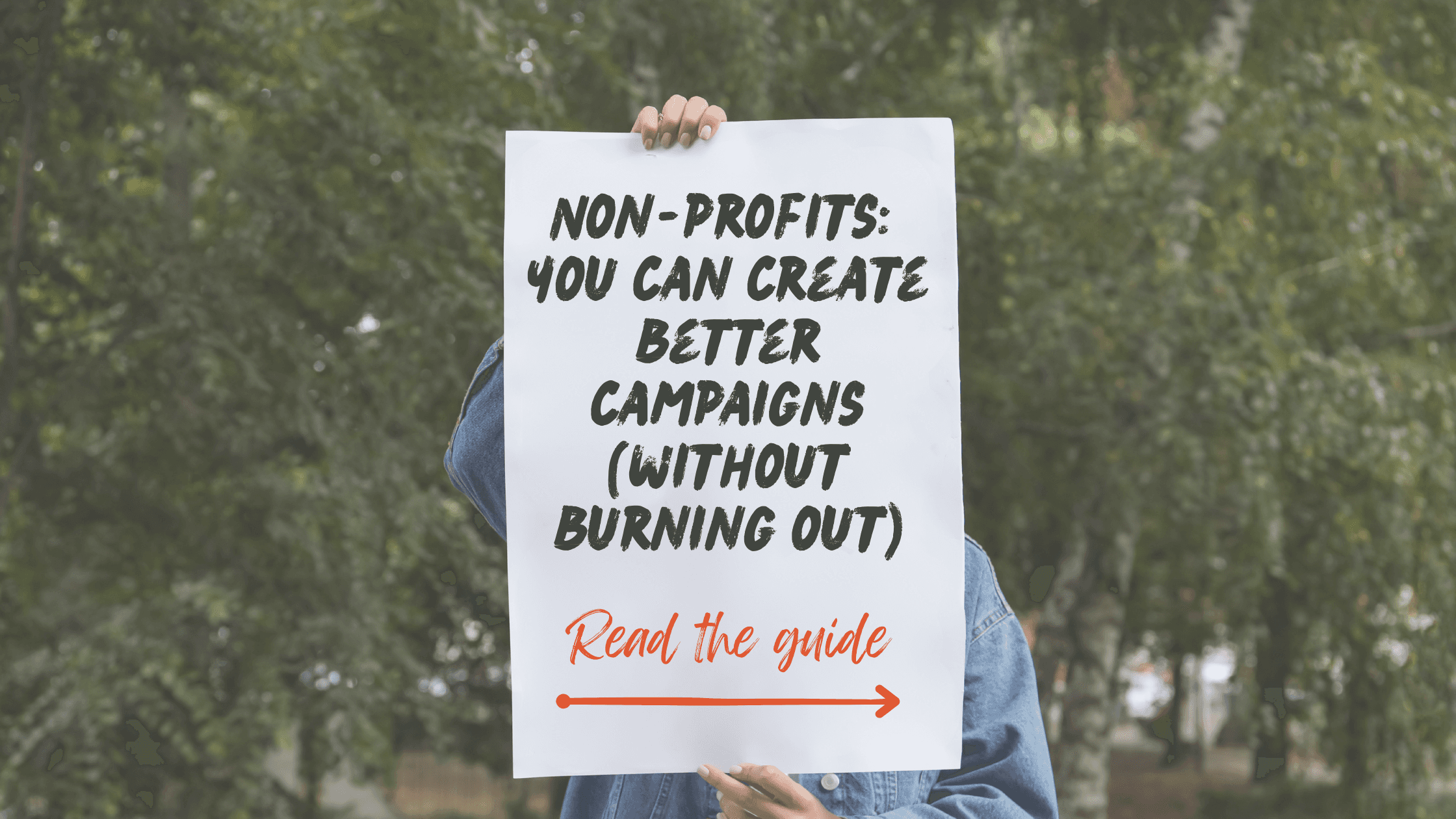 Image of someone holding a white sheet of paper on which is written the following copy: 'Non-profits, you can create better campaigns (without burning out). Underneath there is a red arrow and words: 'read the guide'