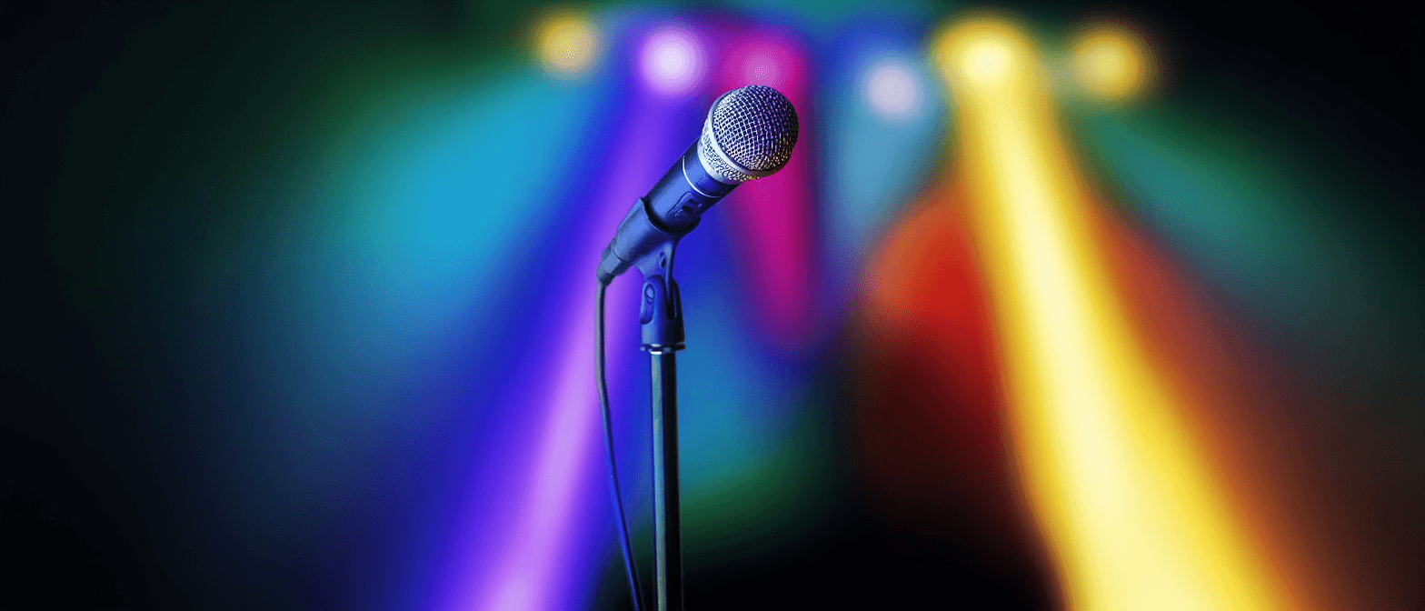 Microphone on stand against a colorful, blurred stage light background.