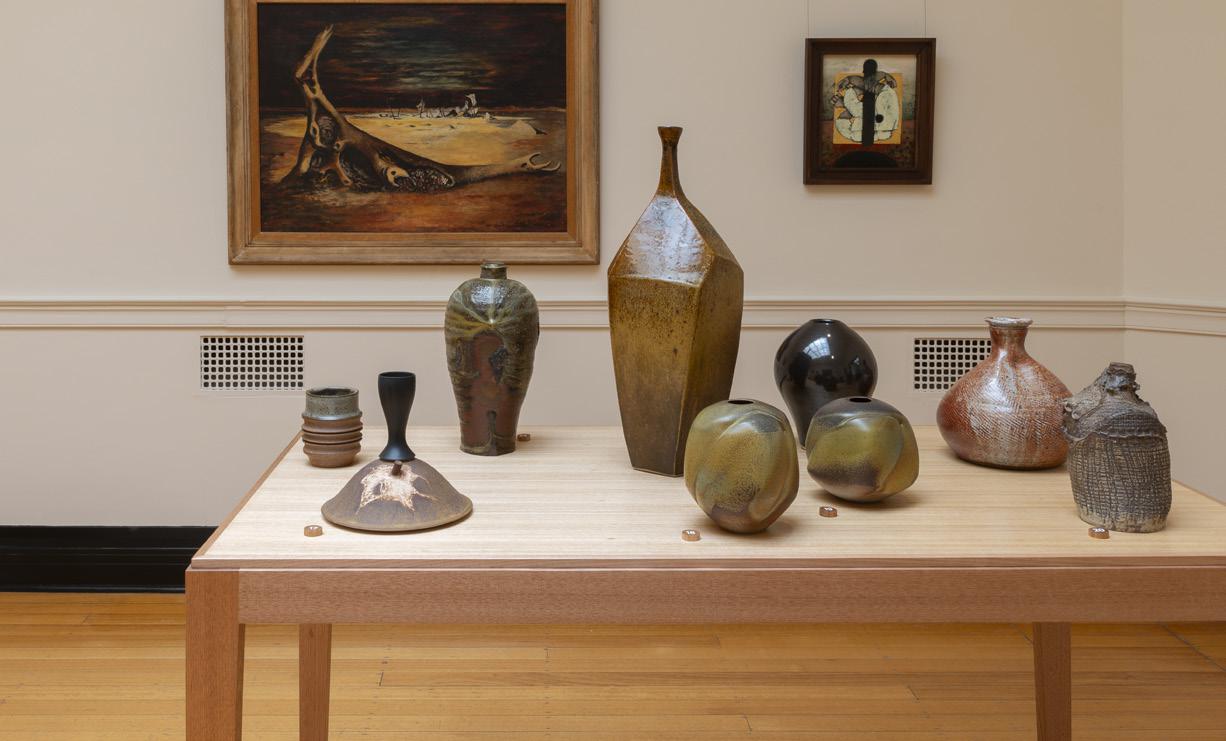 Contemporary ceramic vases on display in an art gallery with framed paintings.