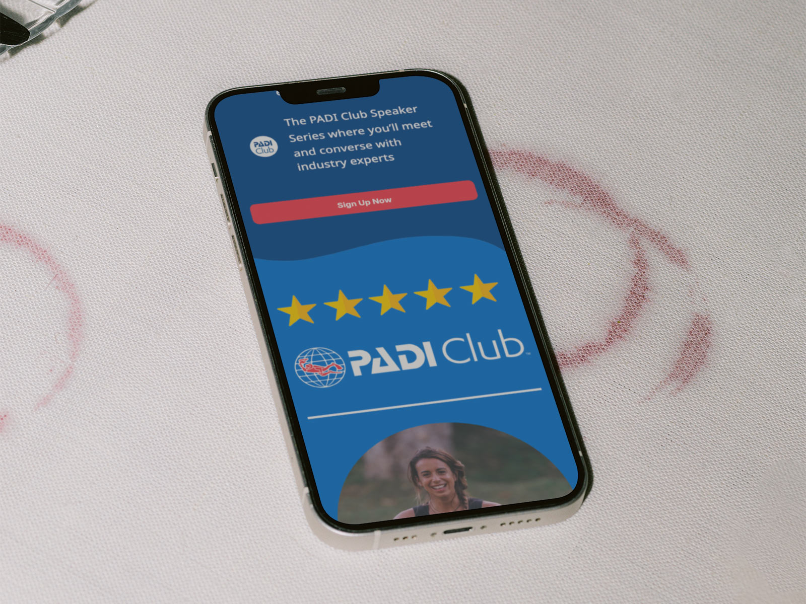 Smartphone mockup displaying a PADI Club promotional email featuring event messaging, branded content modules, and mobile-first membership campaign design on a textured fabric surface.