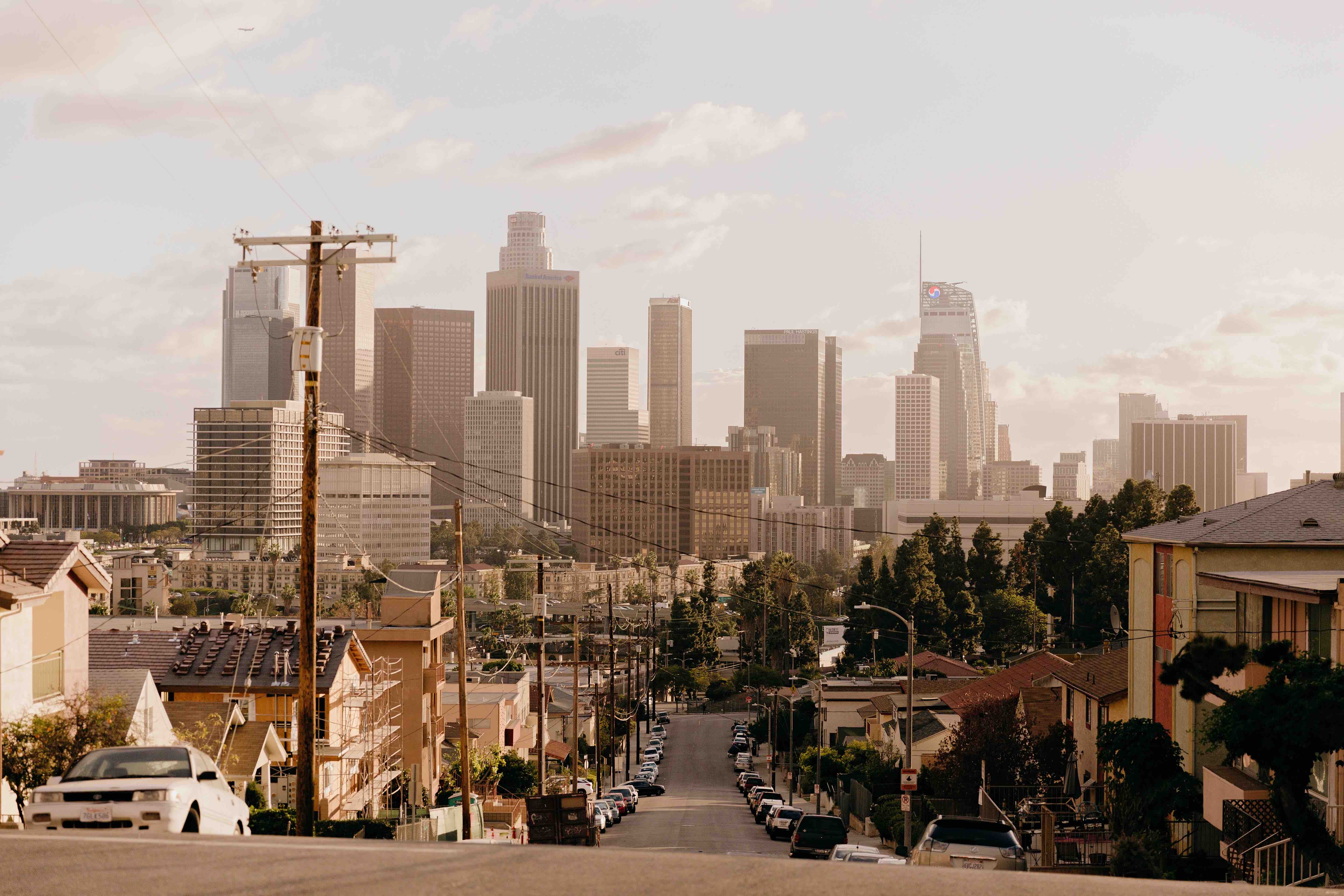 Dreamy view of downtown Los Angeles with the sun glistening through the buildings with golden light, lighting up the sky with a golden glow, taken from the street perspective of a domestic area with houses surrounding