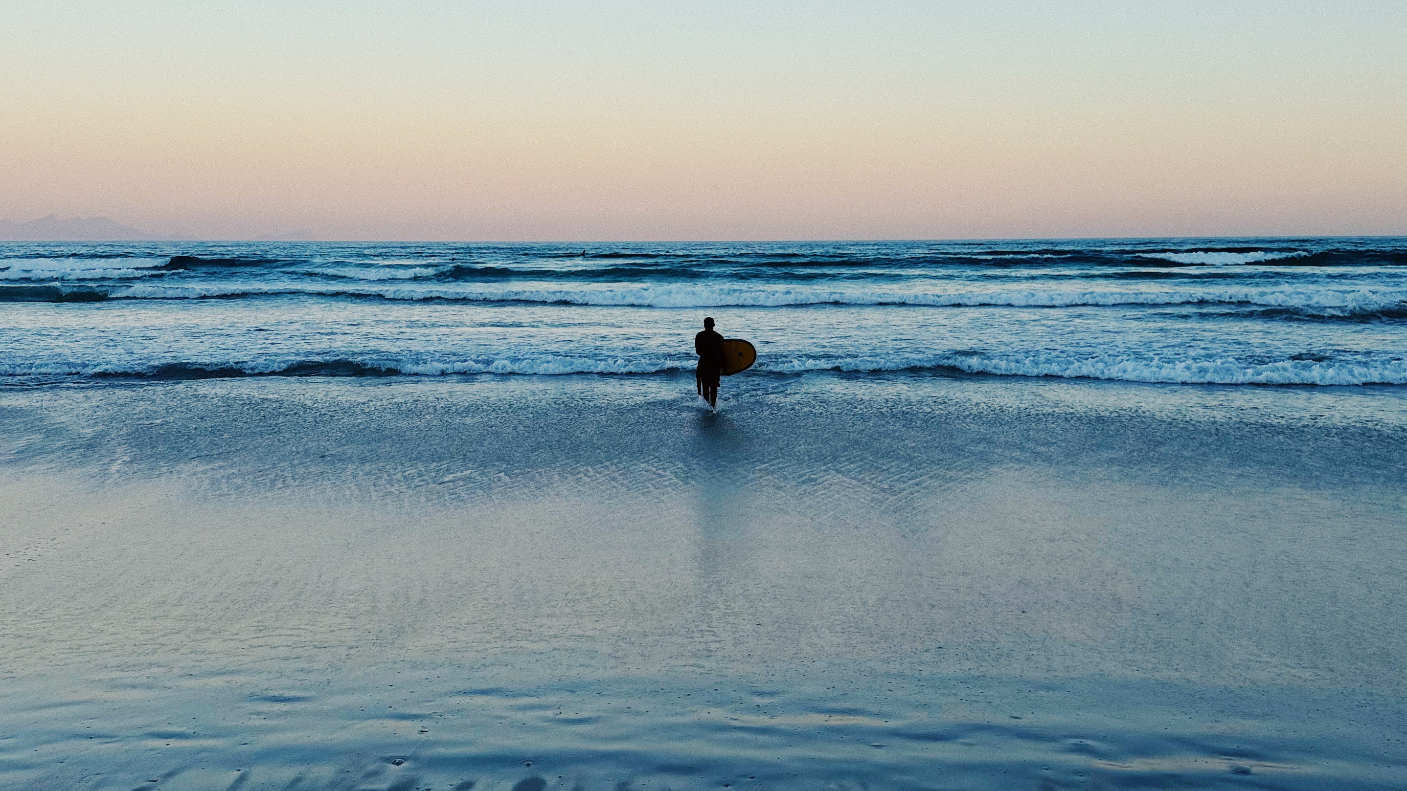 A surfer holding his surfboard while entering the water at Muizenberg beach, Cape Town
