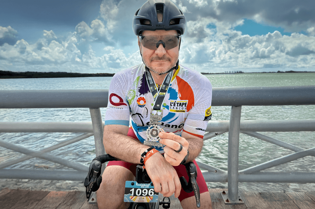 Ciclista sentado en barandal junto al mar mostrando una medalla de segundo lugar del evento.