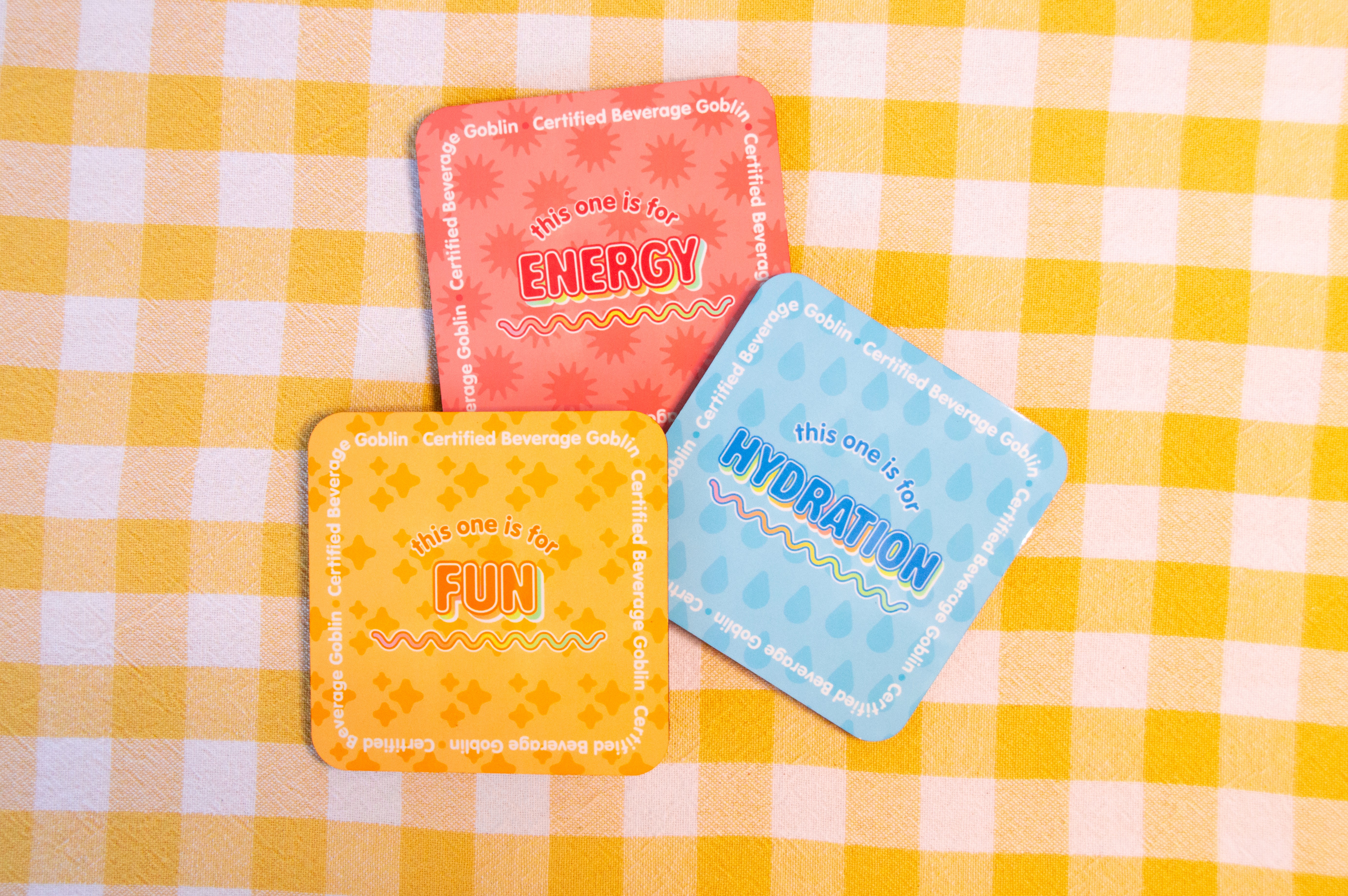 Three drinks coasters are pictured. The first is coral and reads "This one is for Energy"; the second is blue and reads "This one is for Hydration"; the third is yellow and says, "This one is for fun".