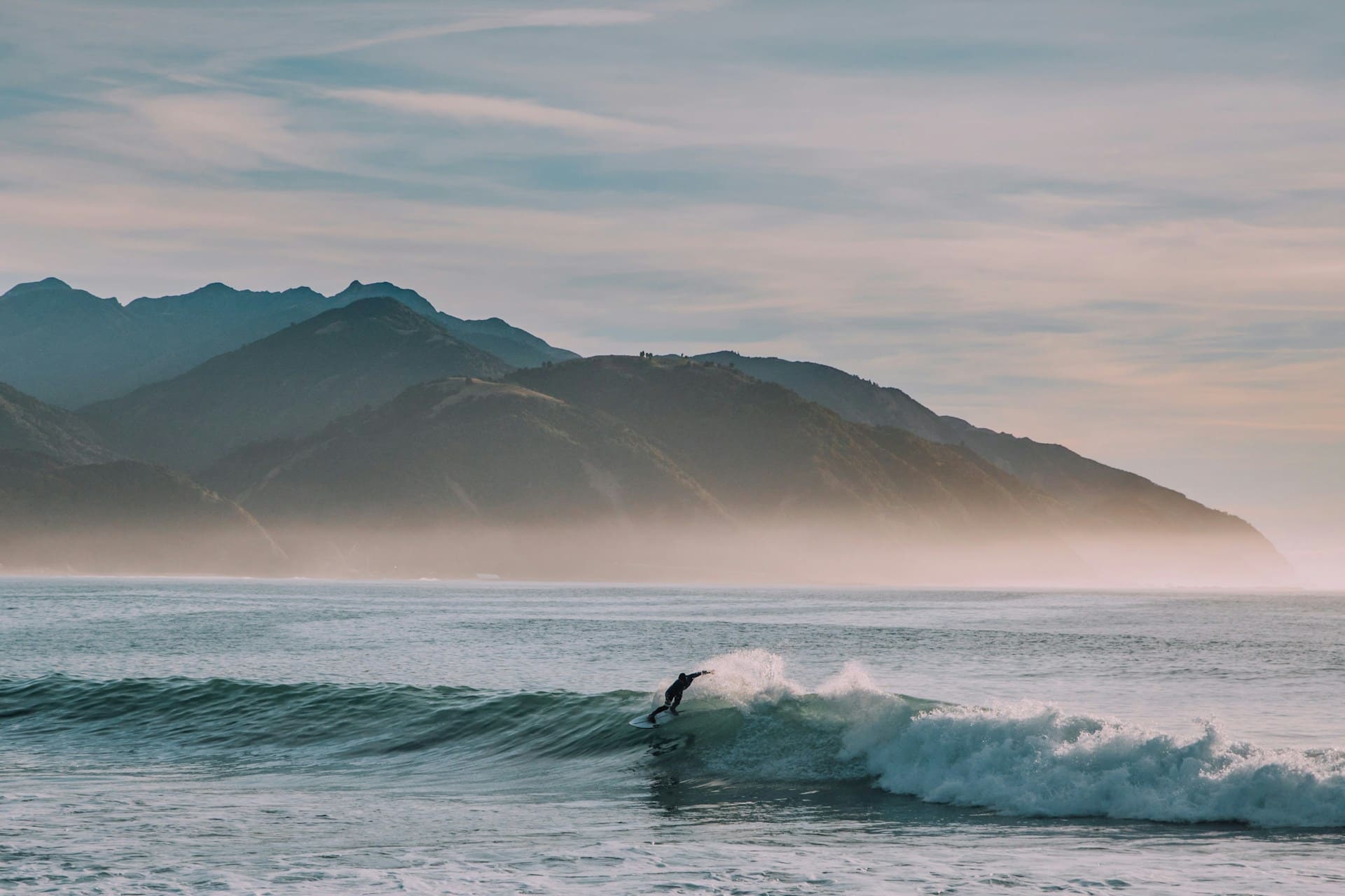 Surfer riding a wave in Portugal with mountains in the background