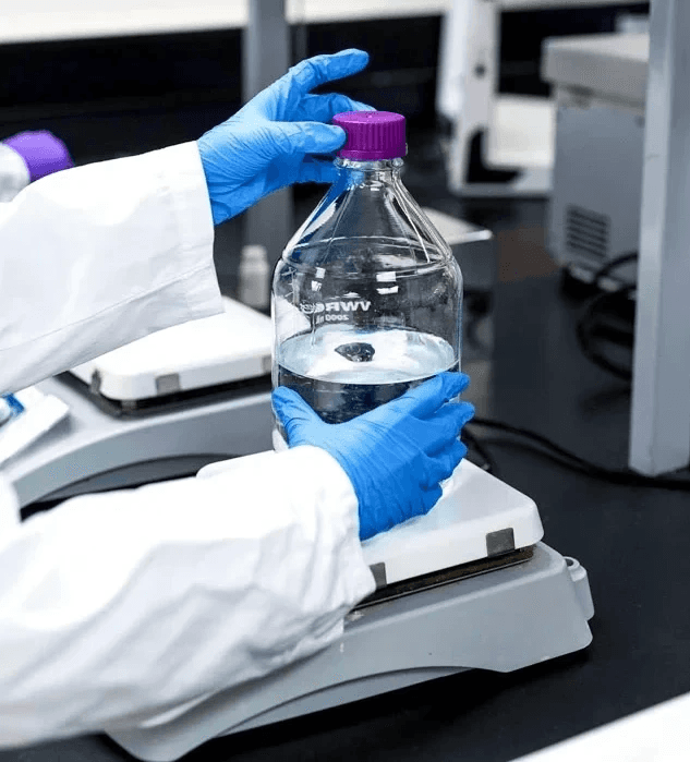 Close-up of a SteriMax scientist in gloves using a scale to weigh a liquid-filled laboratory flask.
