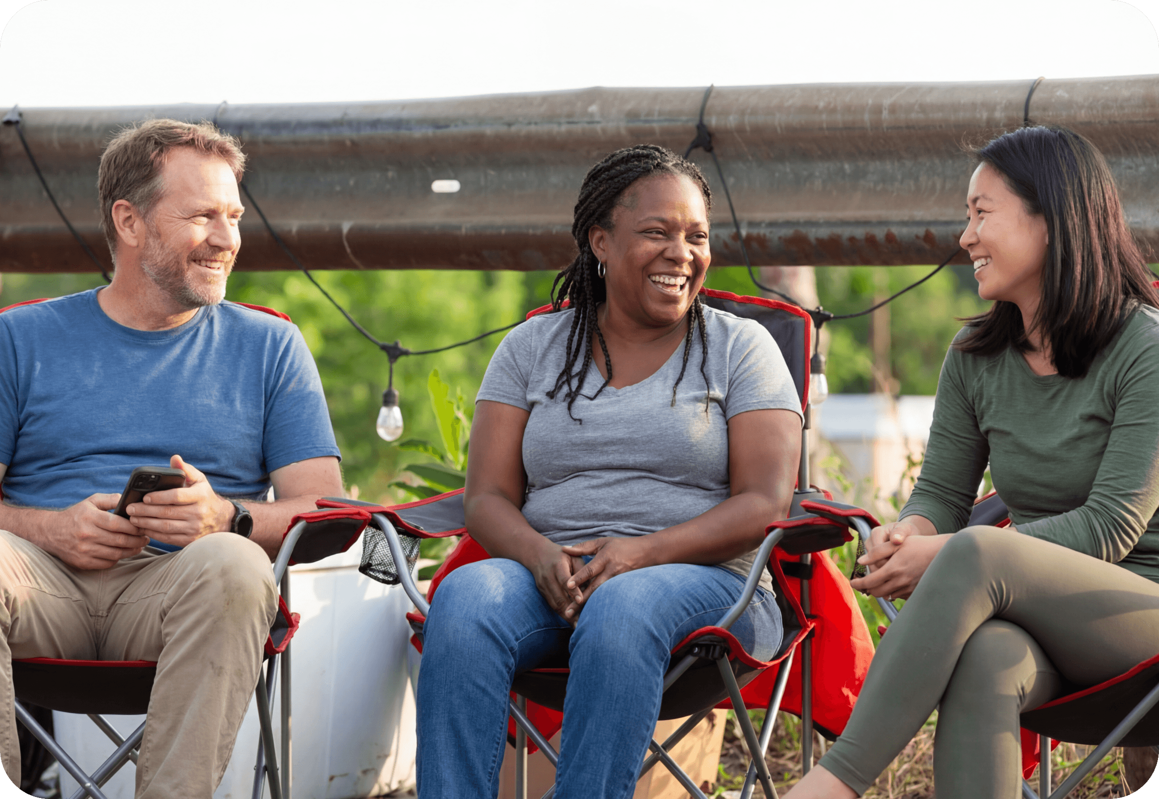hree people sitting together outdoors and talking during a community get-together.