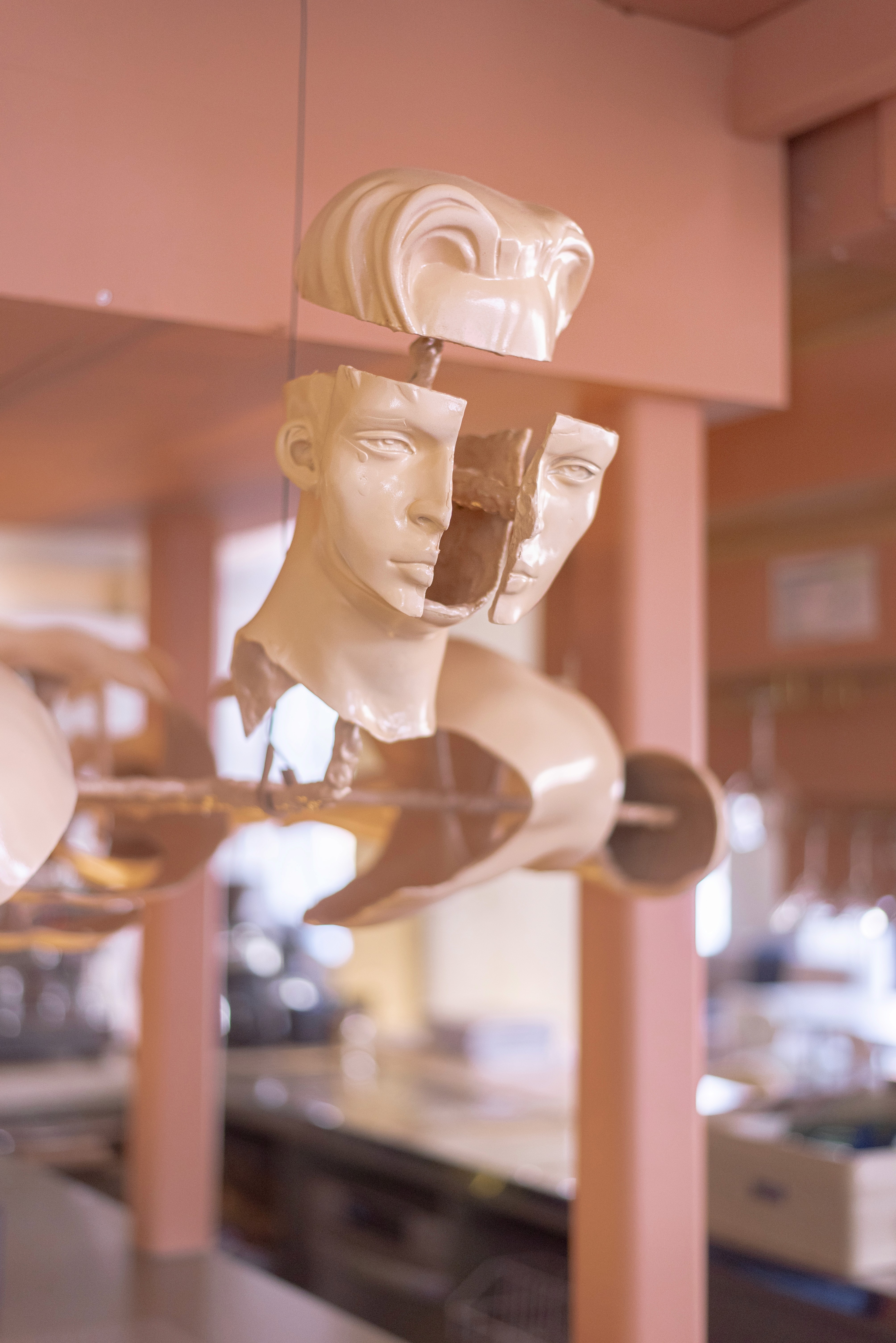 A wooden sculpture of a figure holding another figure, displayed in a light-toned room with minimal decor.