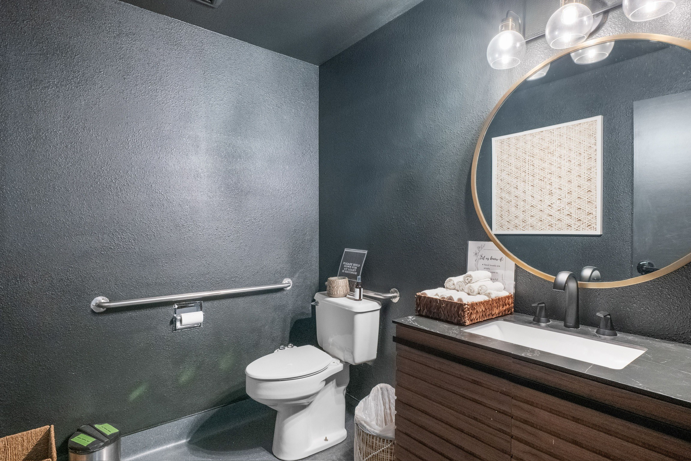 “Modern powder bathroom remodel with dark textured walls, round mirror, and floating wood vanity”
