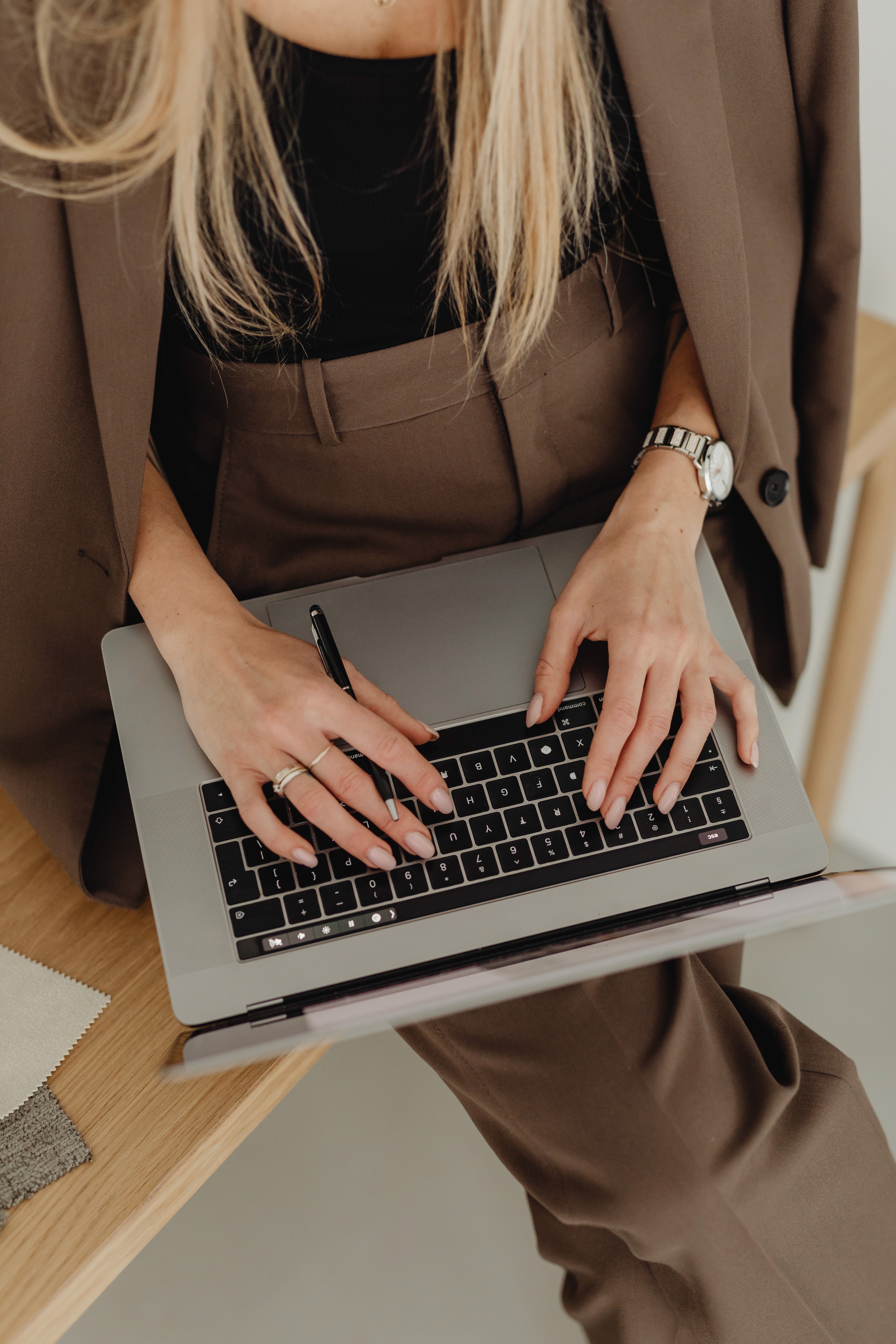 Person in a beige blazer typing on a laptop while seated at a desk, viewed from above.