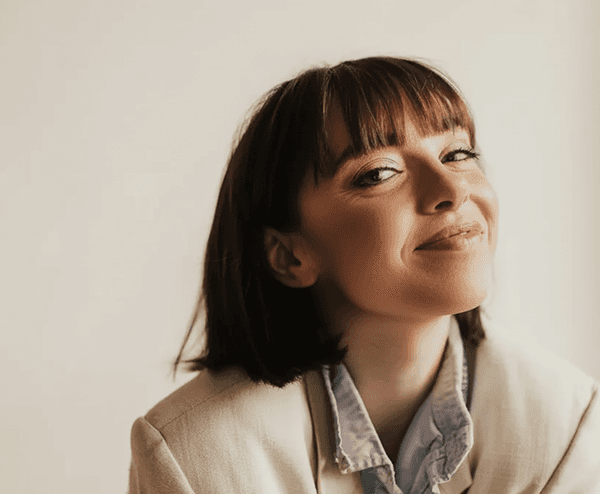 Woman smiling holding phone with provider on screen and a compounded semaglutide bottle next to her.