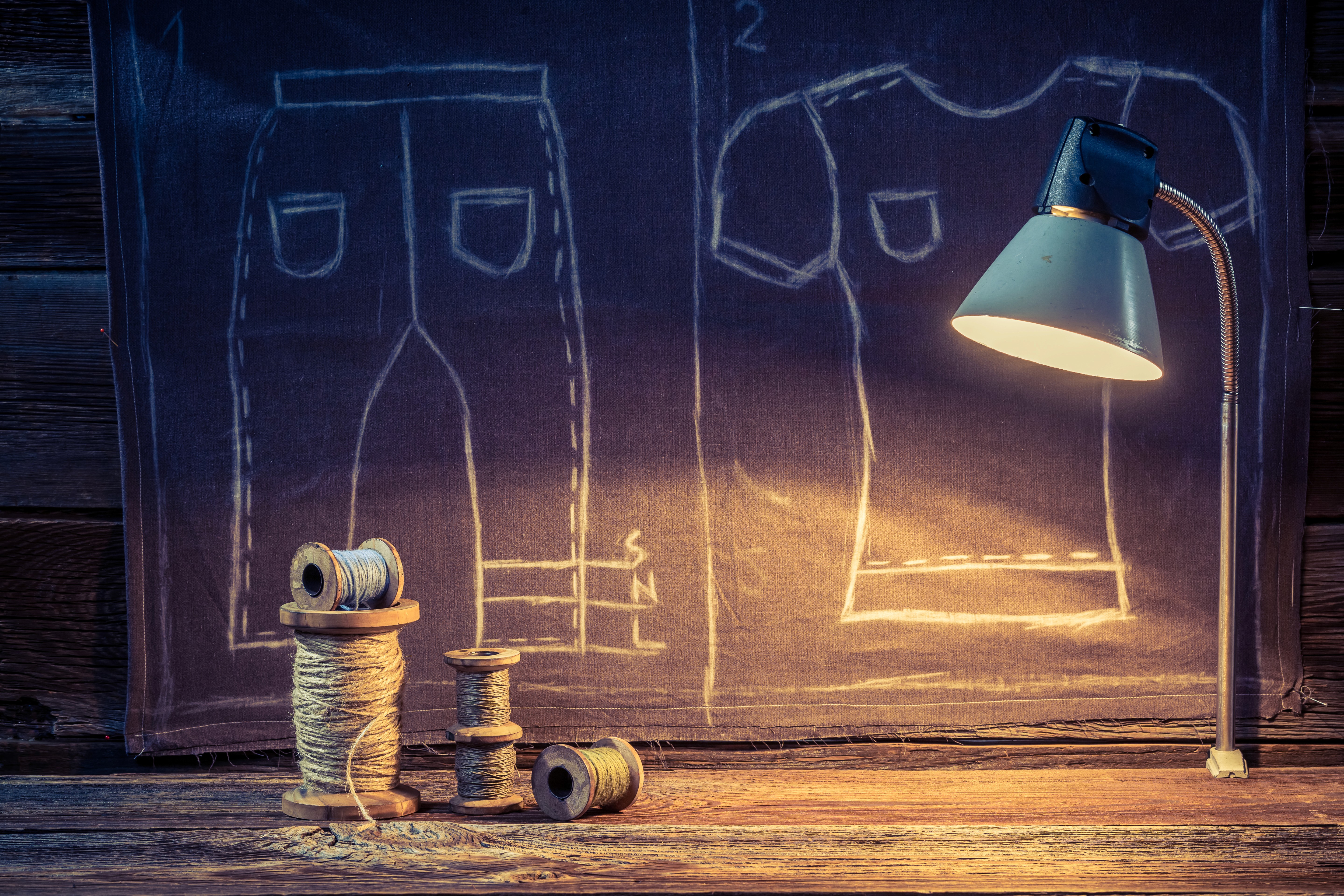 Tailoring workshop scene with thread spools and clothing pattern sketches illuminated by a desk lamp