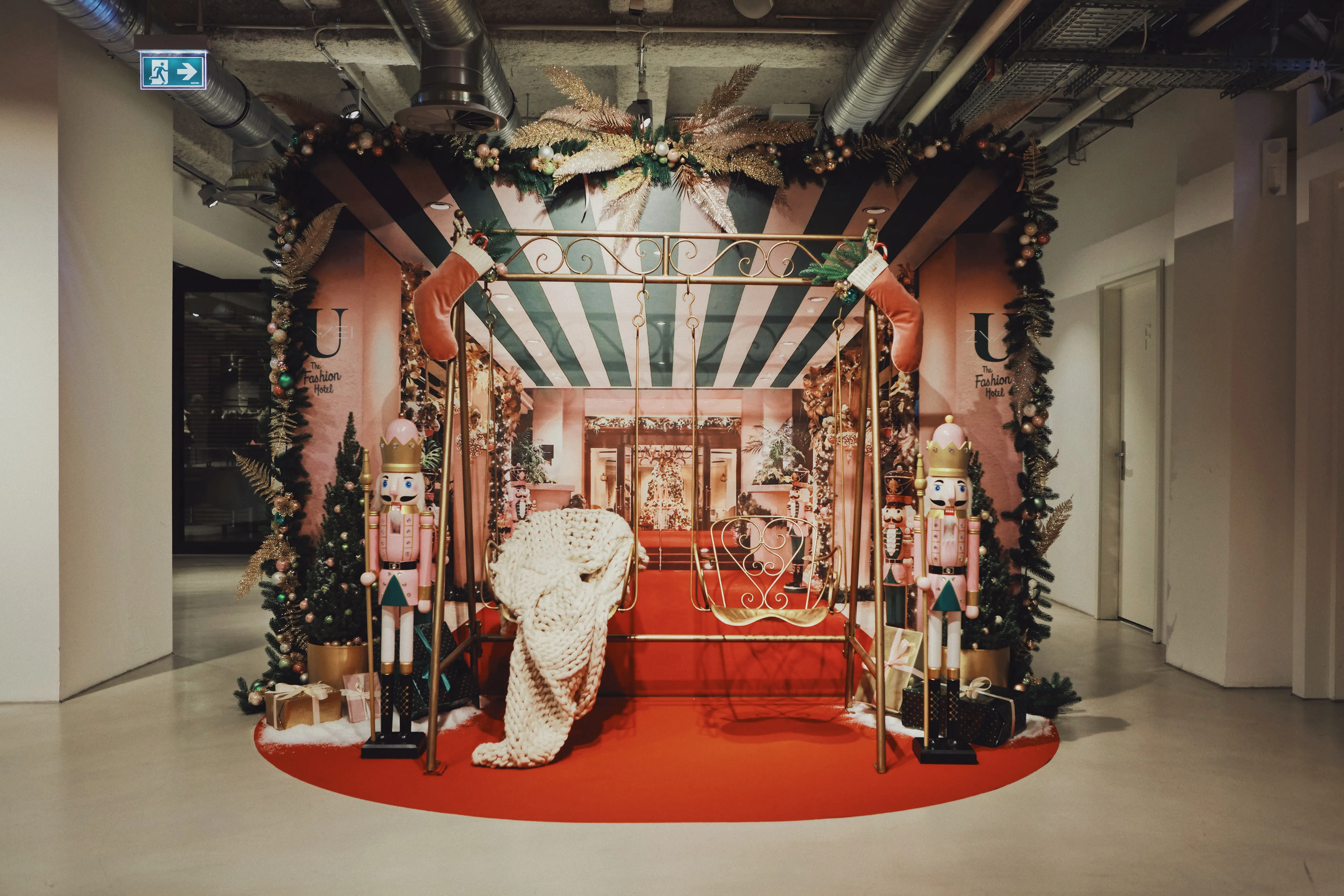 Christmas installation at UZWEI with a striped canopy photo booth, golden swing bench with cosy blanket, two nutcracker figures, garlands and a round red carpet.