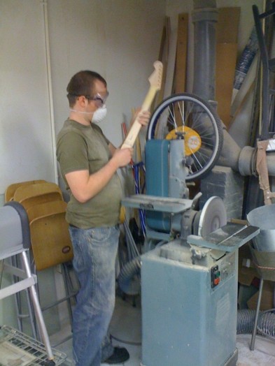 A photo of a man working on a wooden guitar handle in a woodworking workshop.