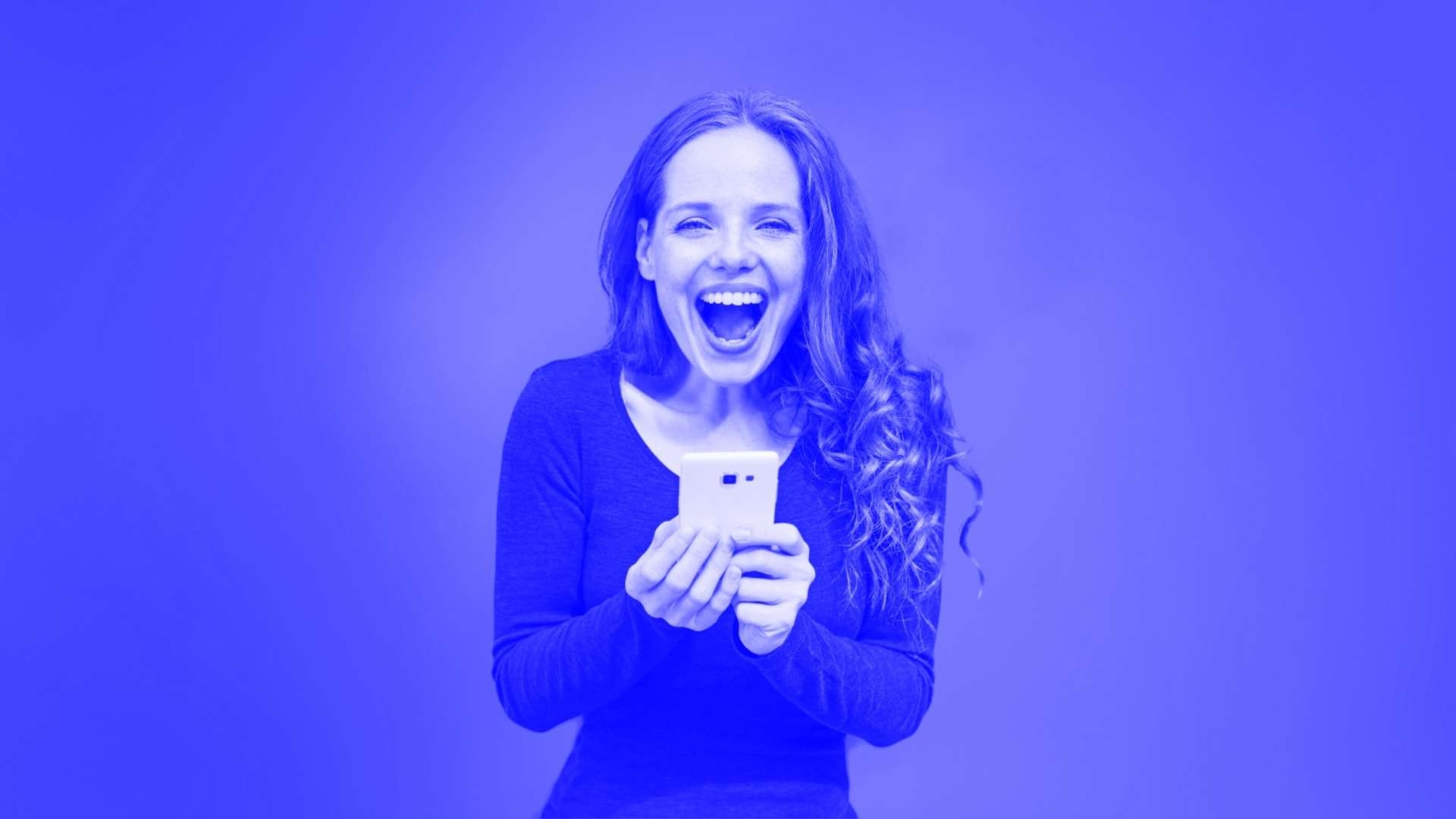 A woman with a big smile on her face holding her mobile phone in front of her