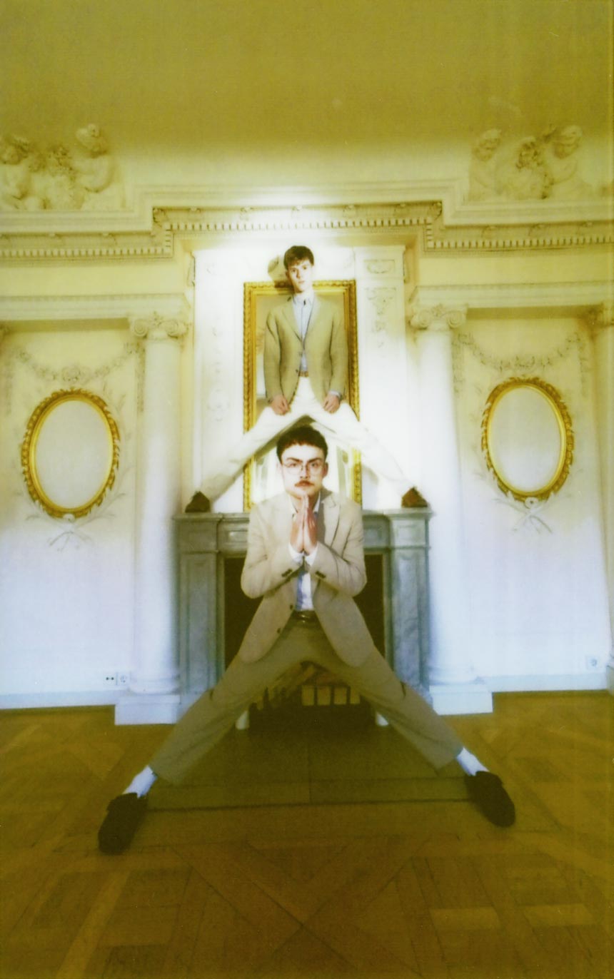 The founders, Dominik Türk and Jonathan Miehlich standing in front and on top of a fireplace, with their legs wide apart.