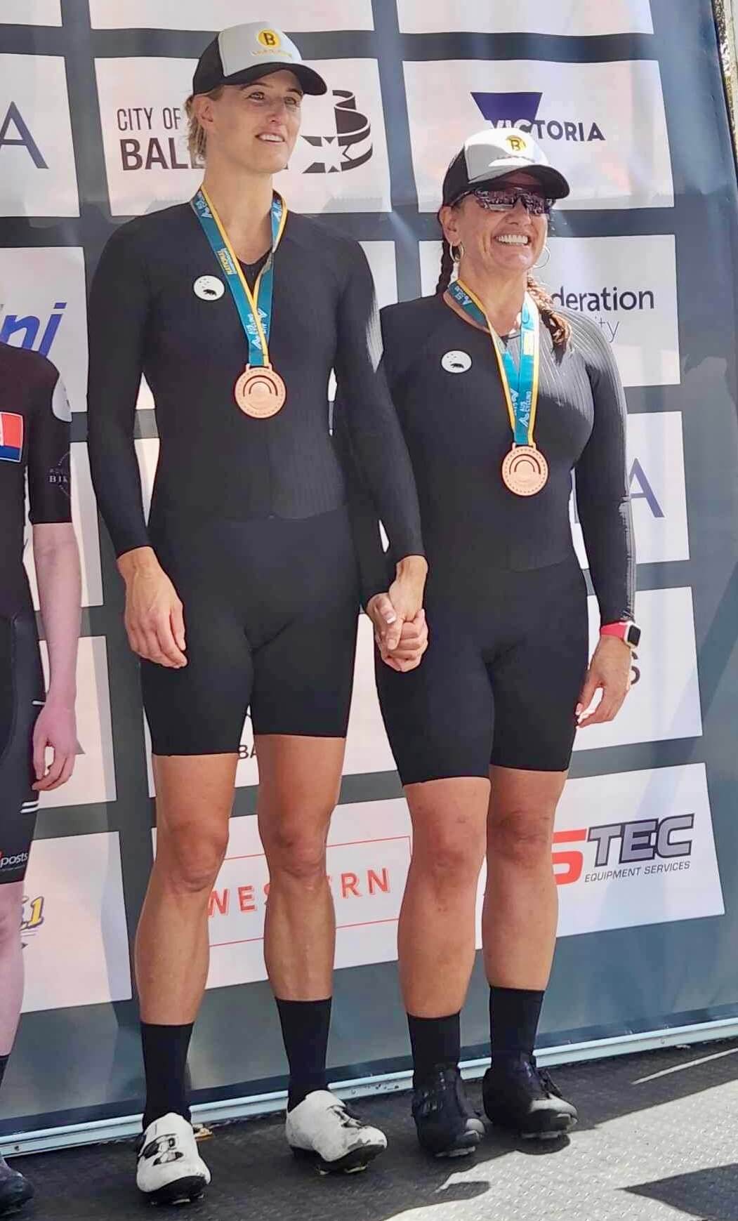 Lily and Jay on-stage, smiling and holding hands with bronze medals around their necks