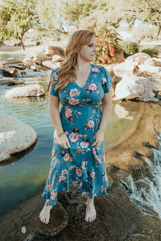 Audra, guest facilitator, standing in a floral dress by a flowing desert stream