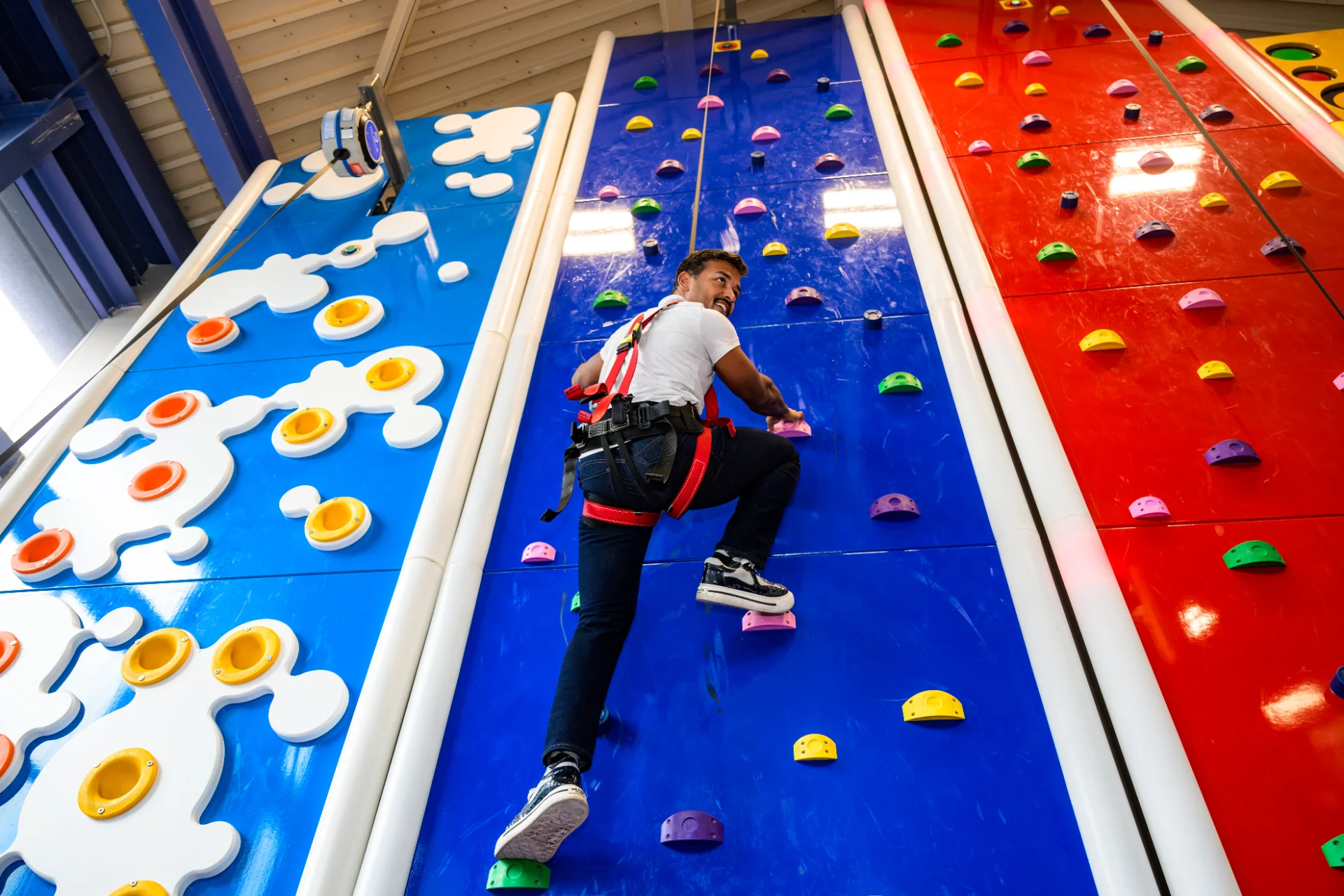 Climber in a harness scaling a blue Clip n Climb wall at LiggettVille
