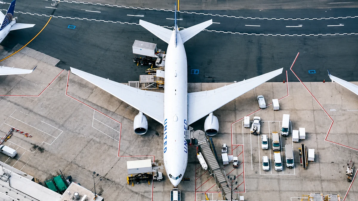 Overhead view of a commercial aircraft surrounded by ground service vehicles and cargo-handling equipment at an airport apron.