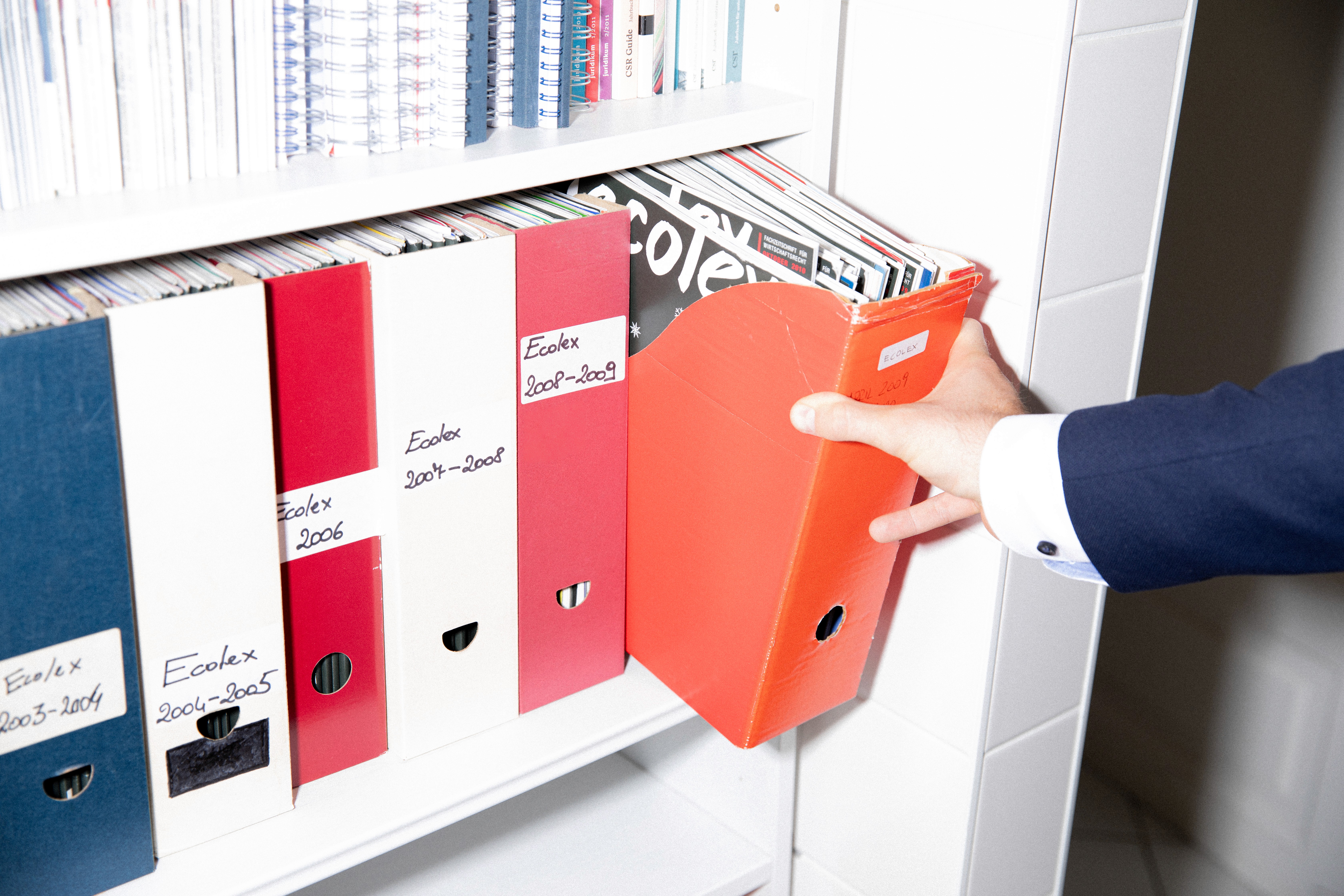 A black and white photo of a basketball hoop with a ball caught in the net, viewed from below against a plain sky