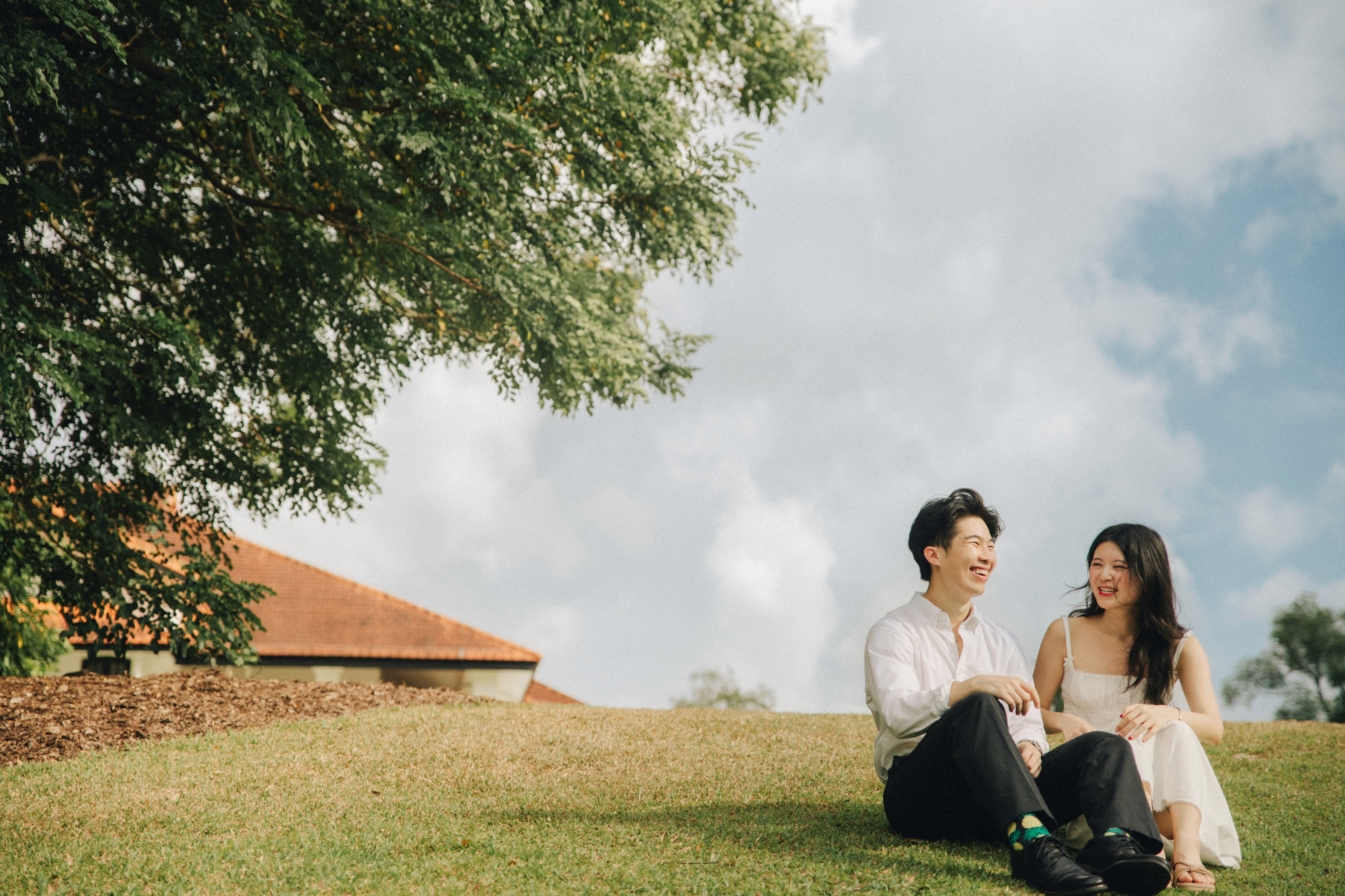 A couple enjoying a quiet moment on the grass after the graduation ceremony, peaceful setting.

